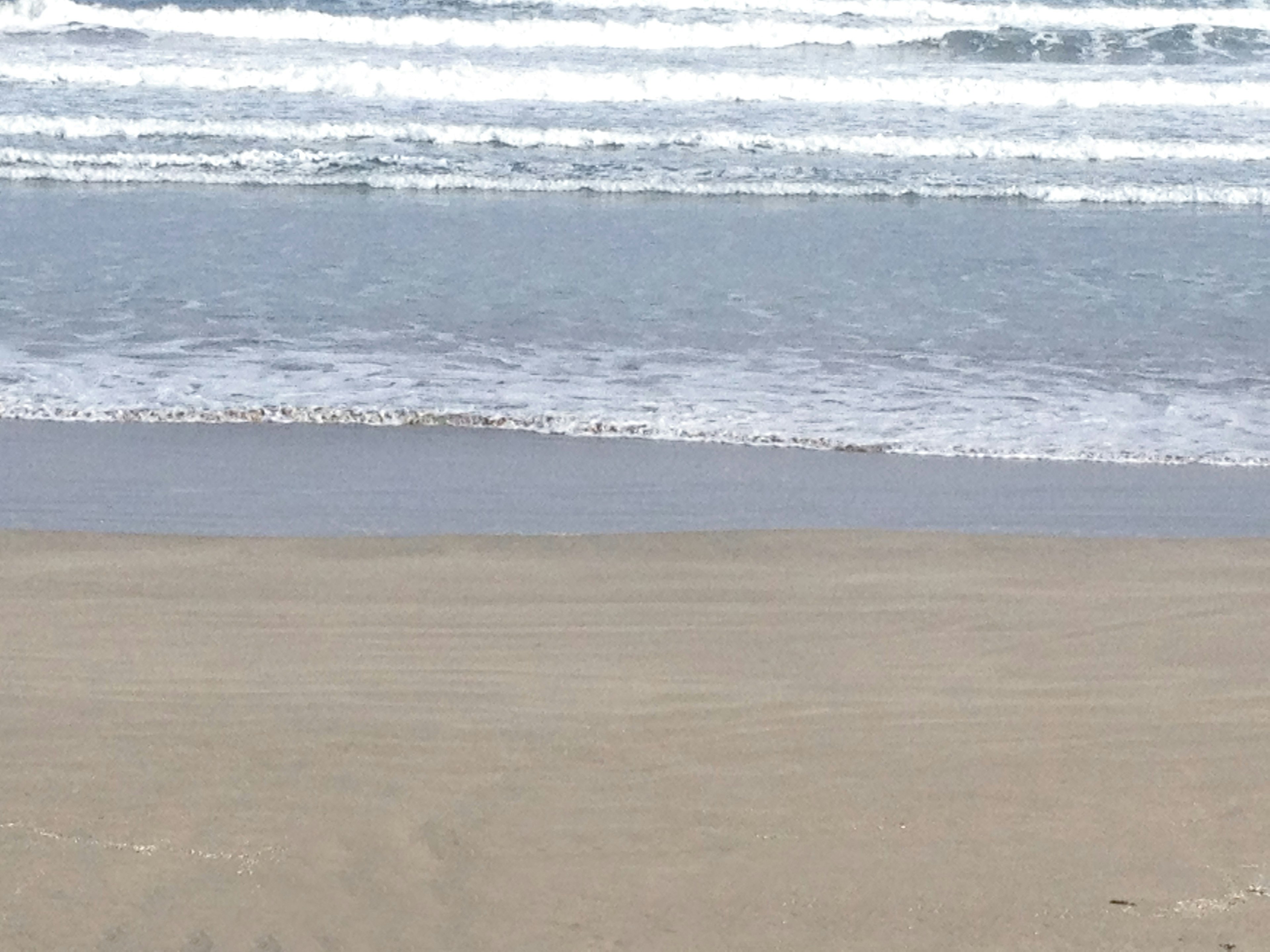 Pemandangan pantai tenang dengan ombak lembut yang menyentuh tepi