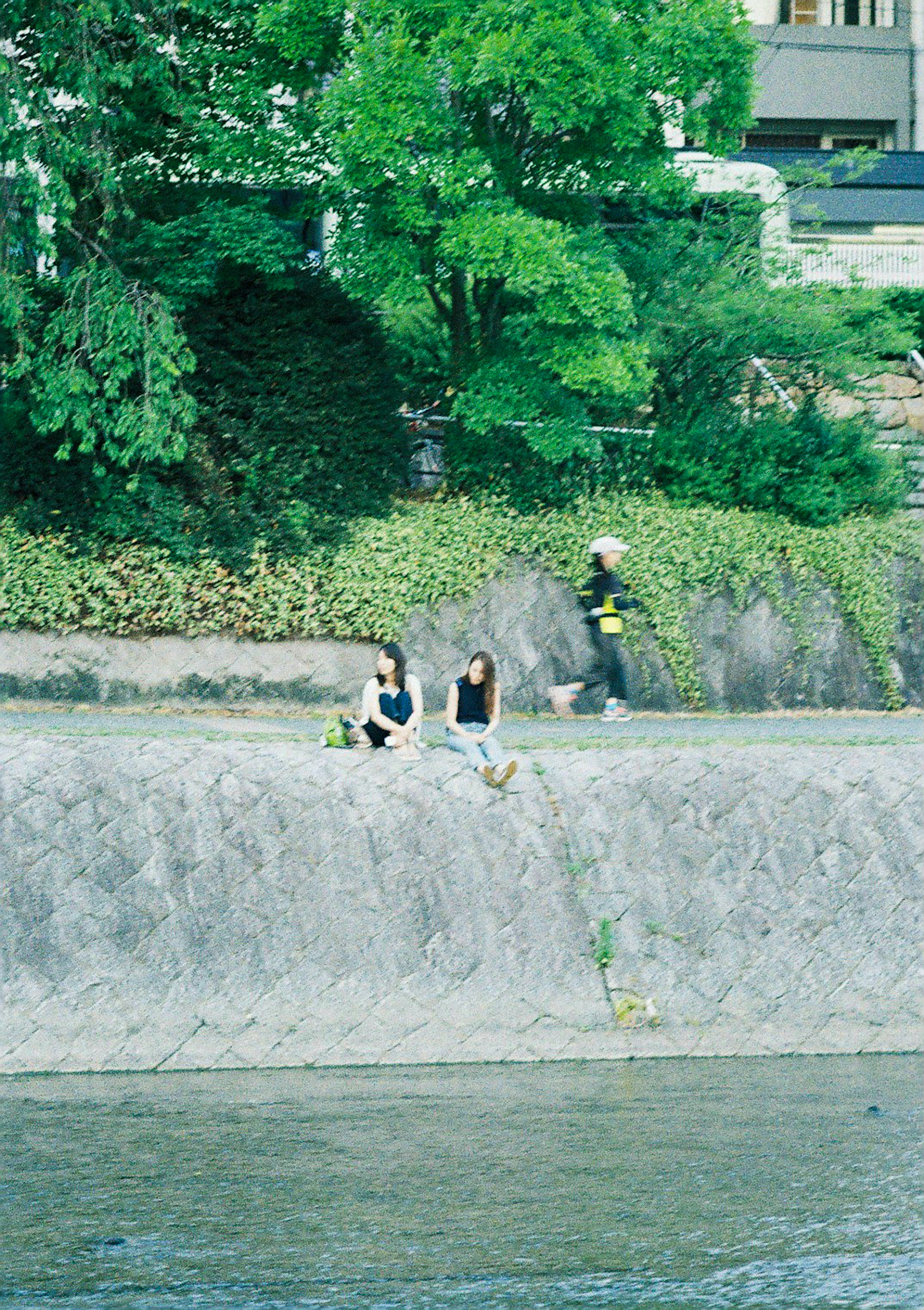 Dos mujeres sentadas junto al río y una persona caminando