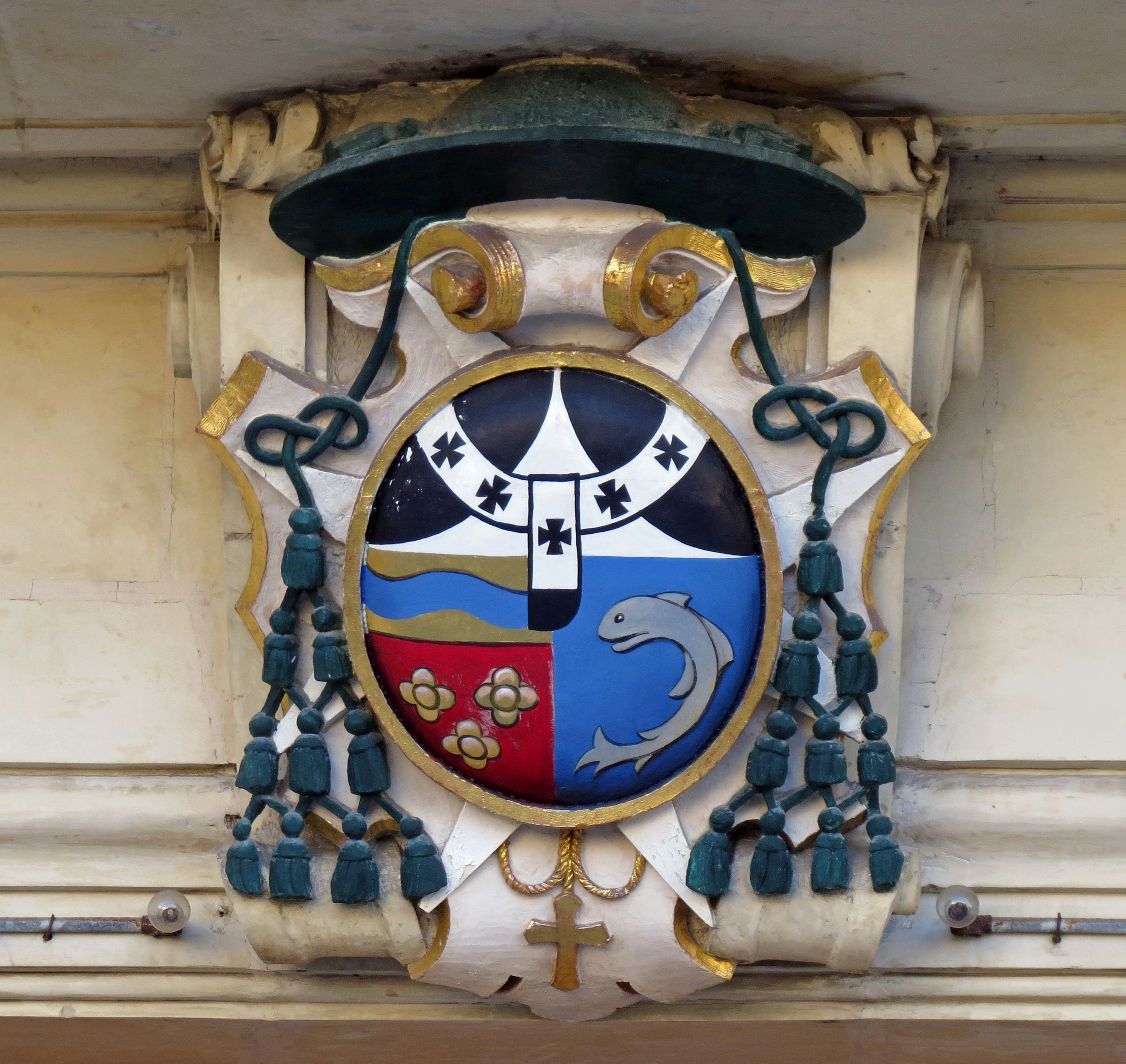 Blason avec un dauphin et des motifs floraux sur un bouclier bleu orné de décorations dorées et de rubans verts