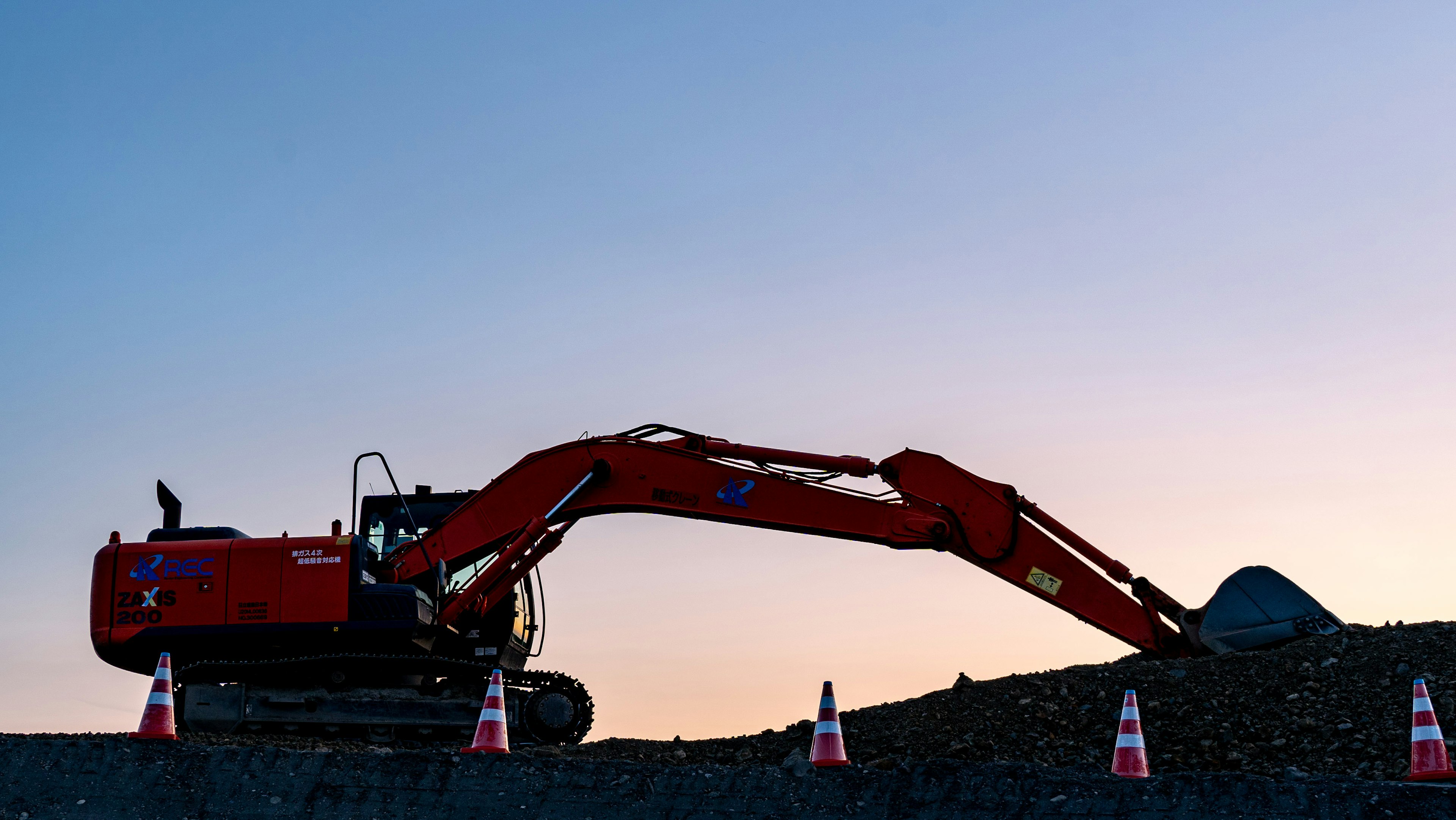 Siluet dari ekskavator merah yang bekerja di bawah langit senja