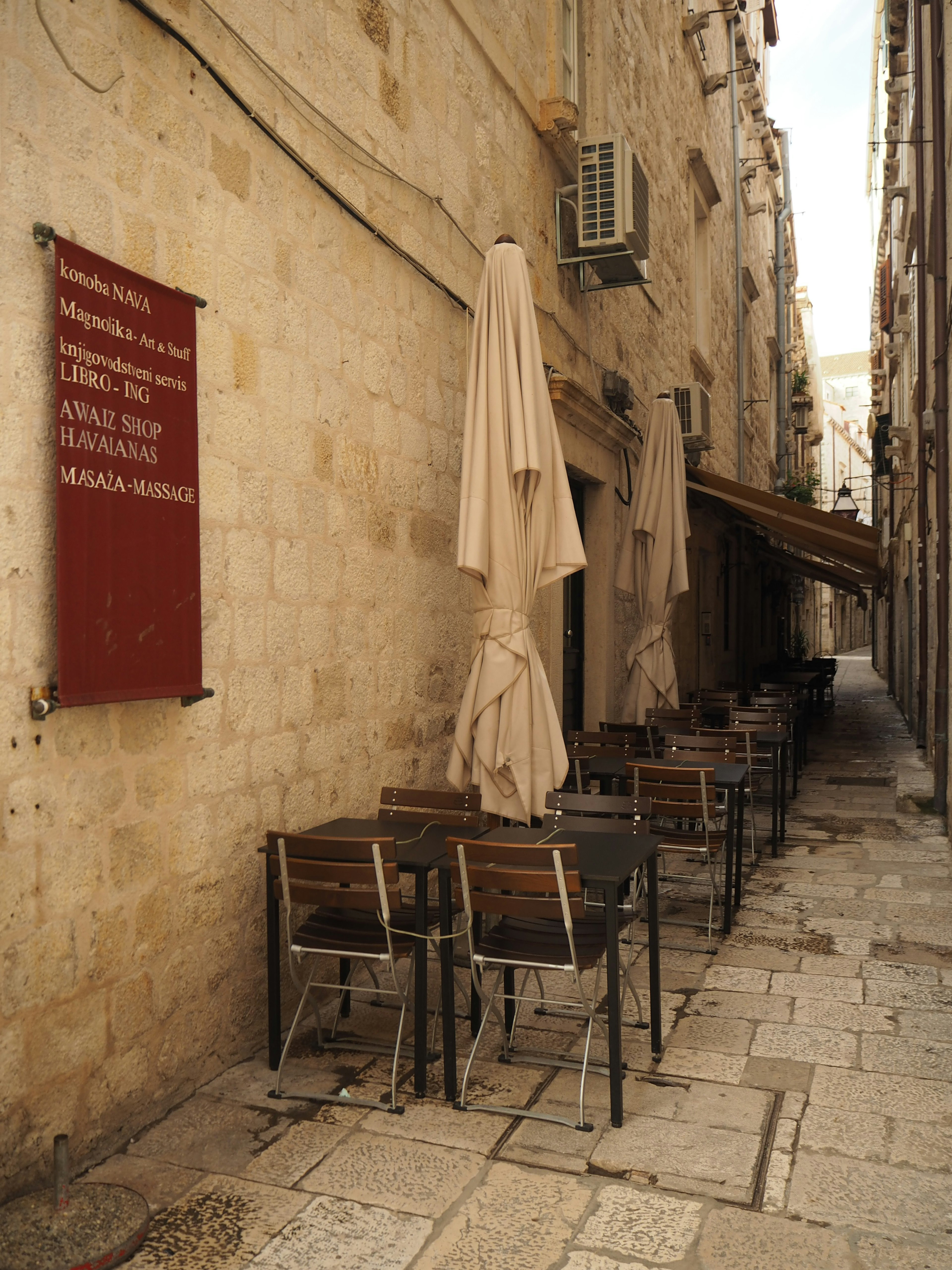 Narrow alley lined with tables and chairs featuring umbrellas for shade