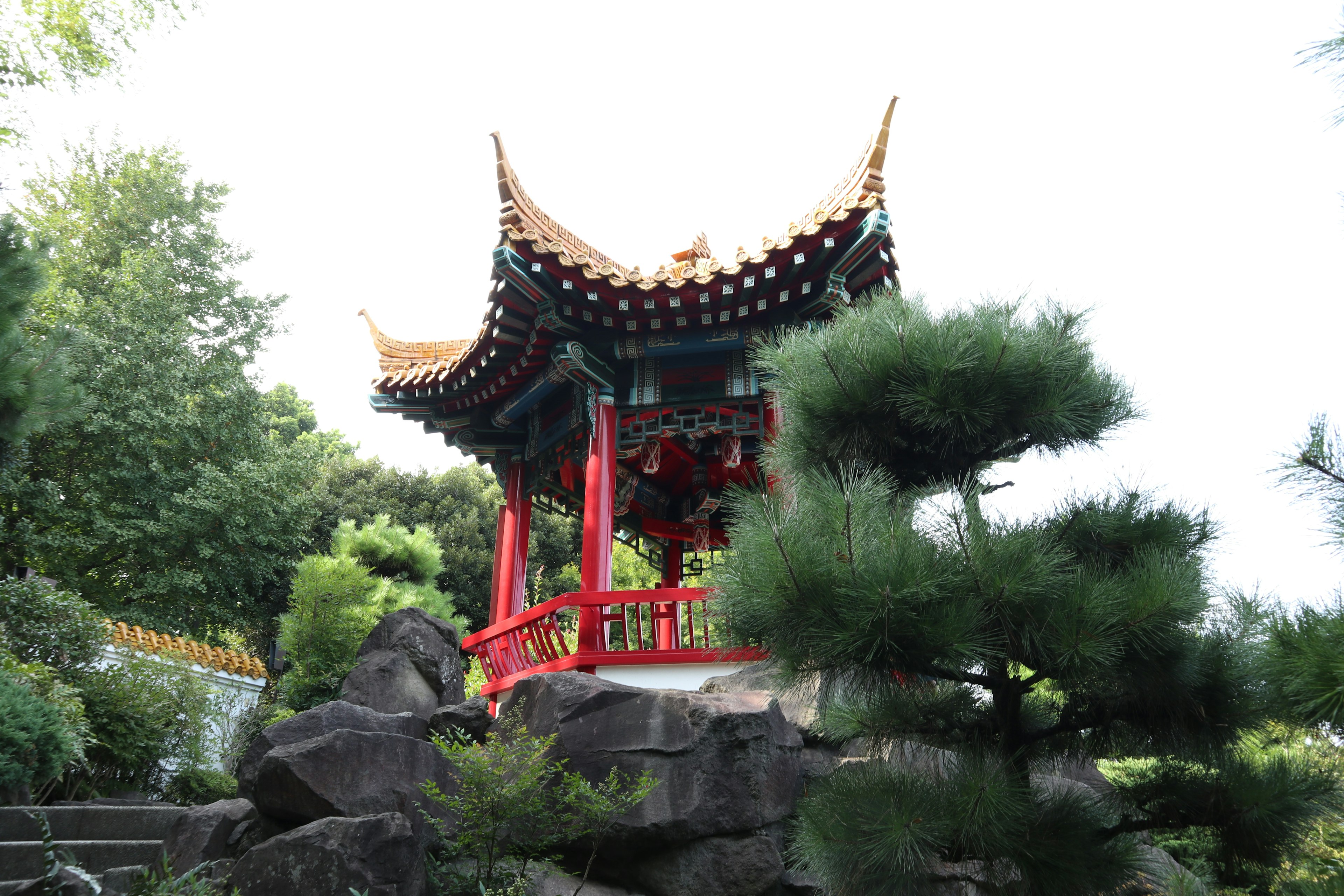 Pavillon chinois avec des piliers rouges et un toit entouré de verdure