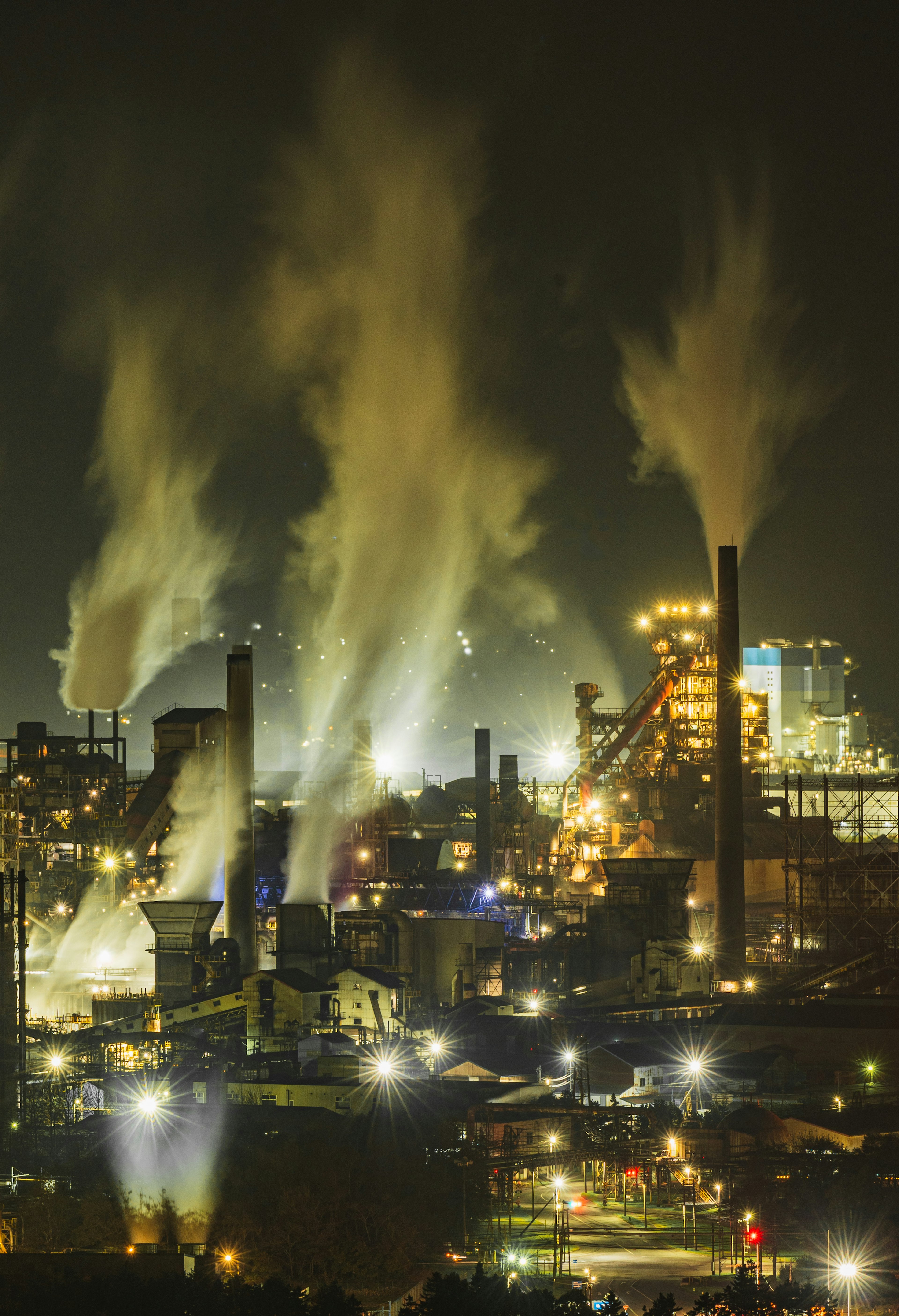 Paesaggio industriale notturno con camini che rilasciano vapore e luci brillanti