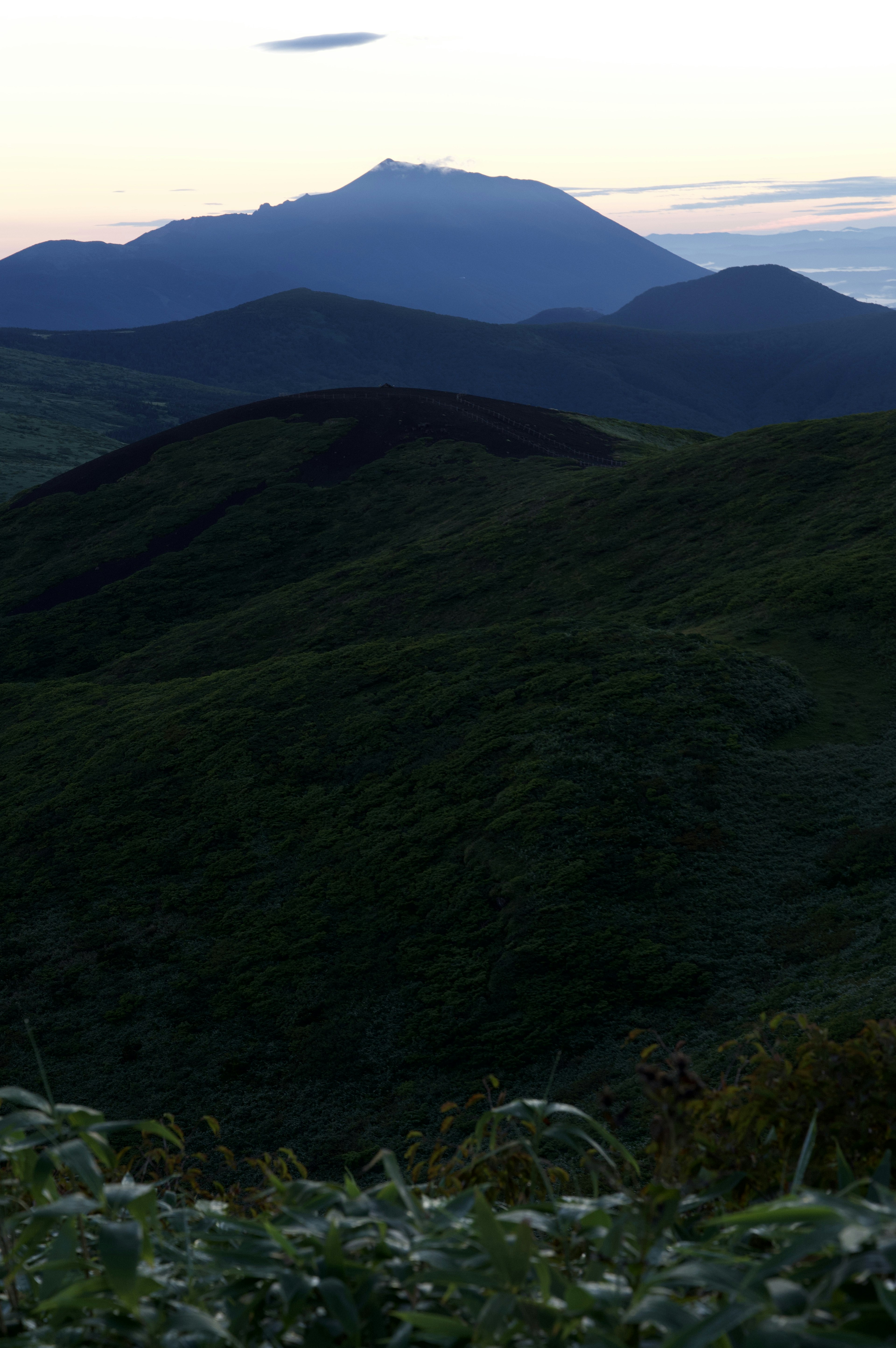 Colinas verdes con silueta de montaña a lo lejos al atardecer