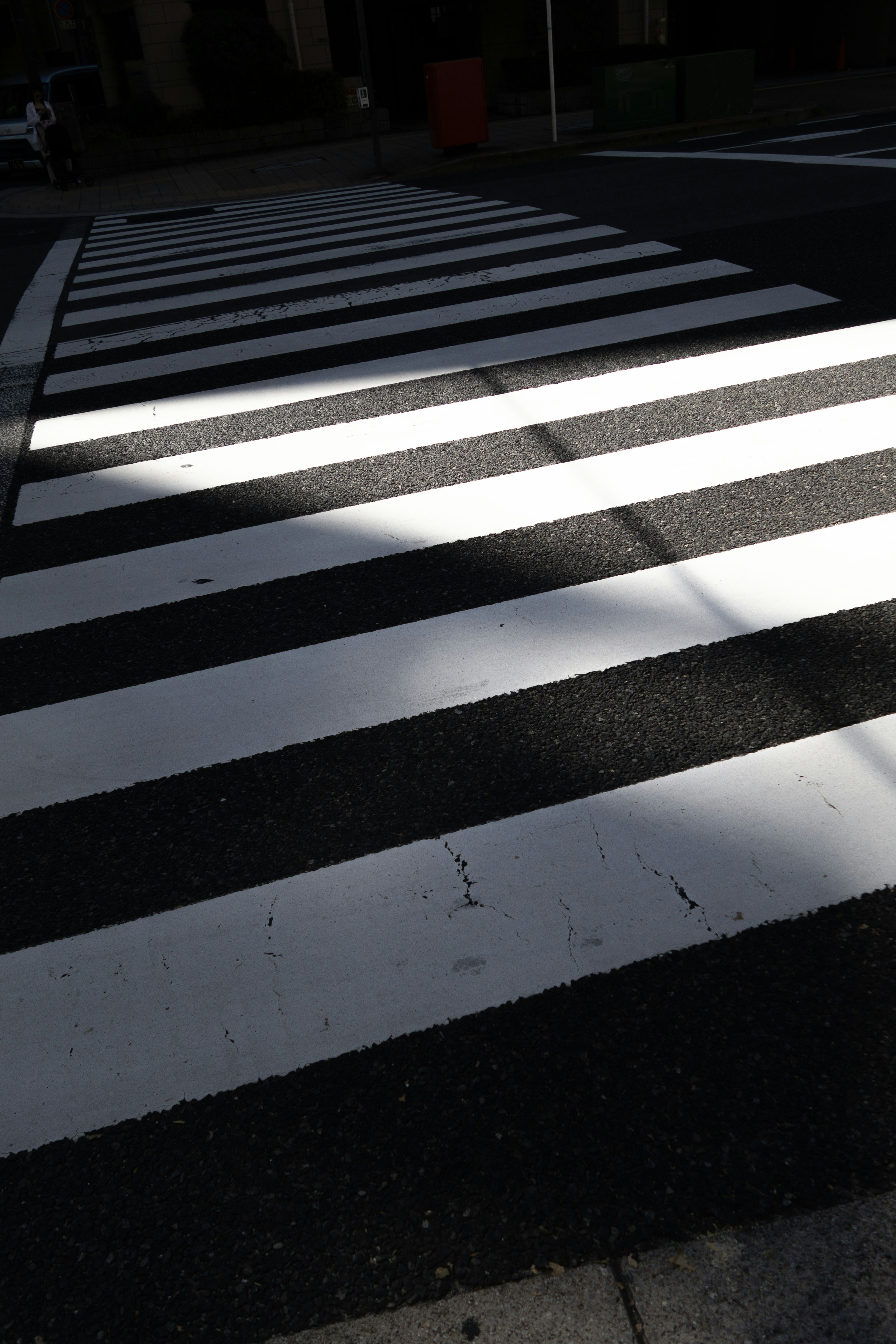 Una foto de un paso de peatones de rayas blancas y negras con contraste de luz y sombra