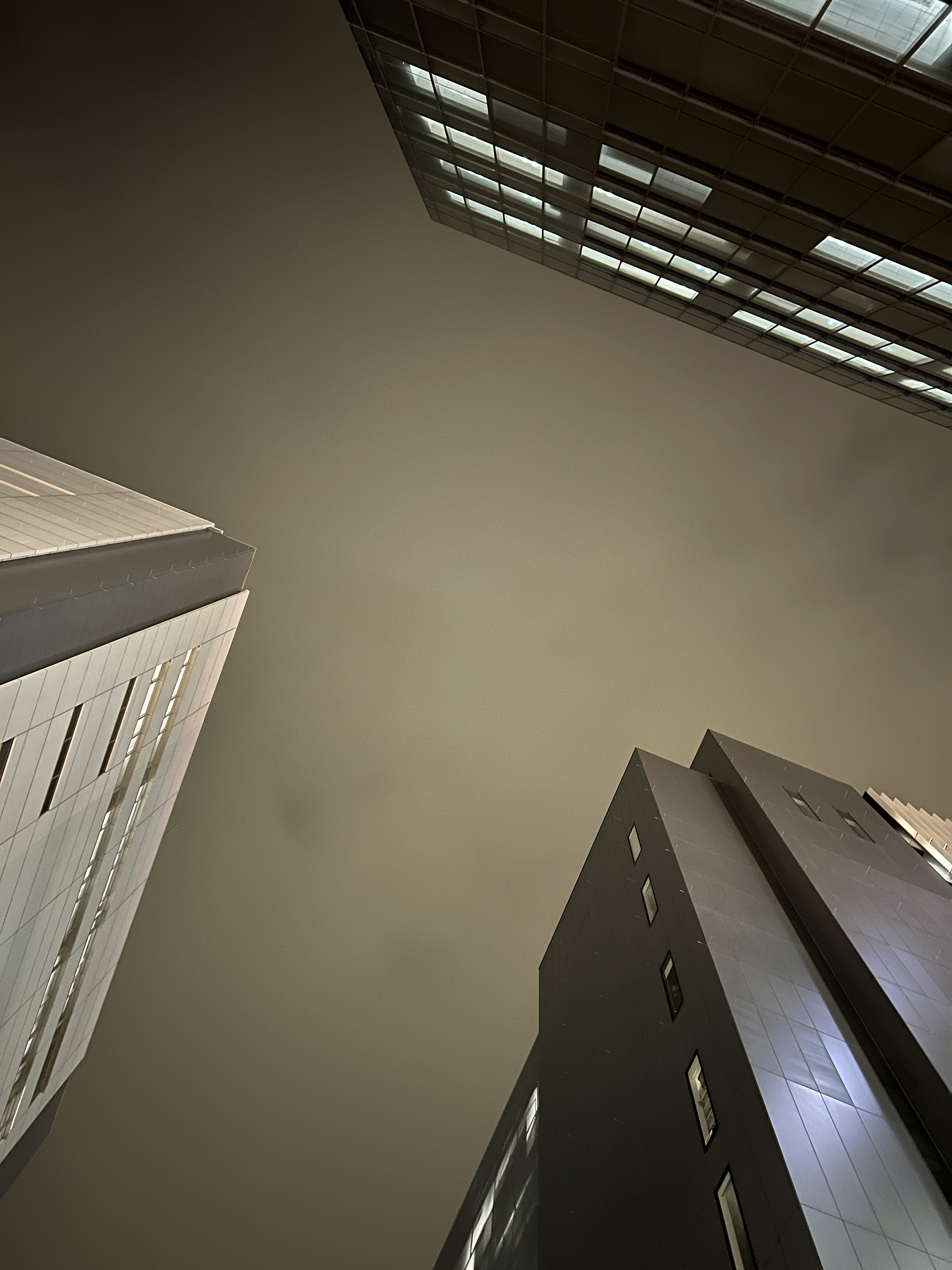 Foto mirando hacia el cielo nocturno entre edificios Ventanas brillantes contrastan con estructuras oscuras