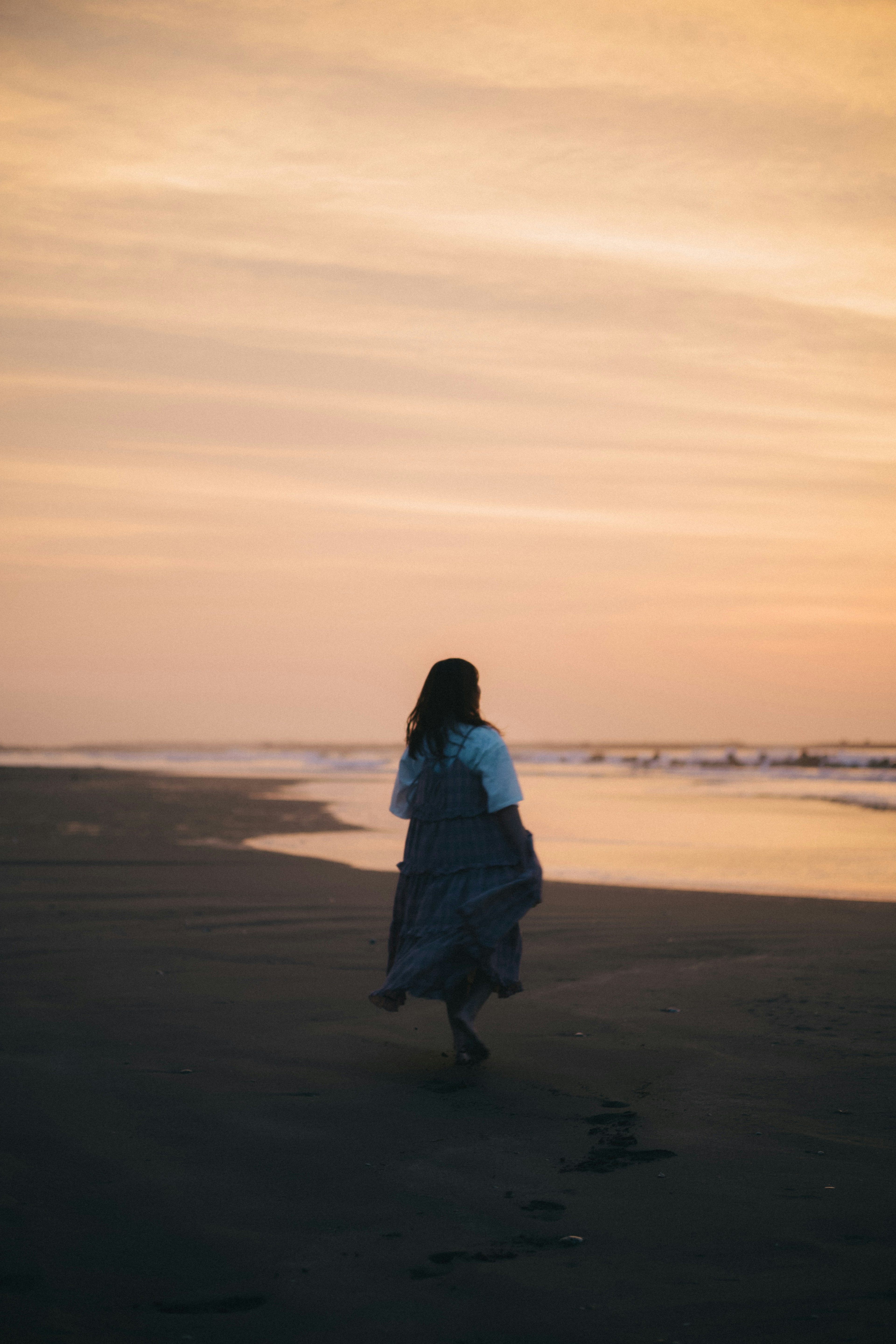 Silhouette seorang wanita berjalan di pantai dengan langit senja yang berwarna-warni