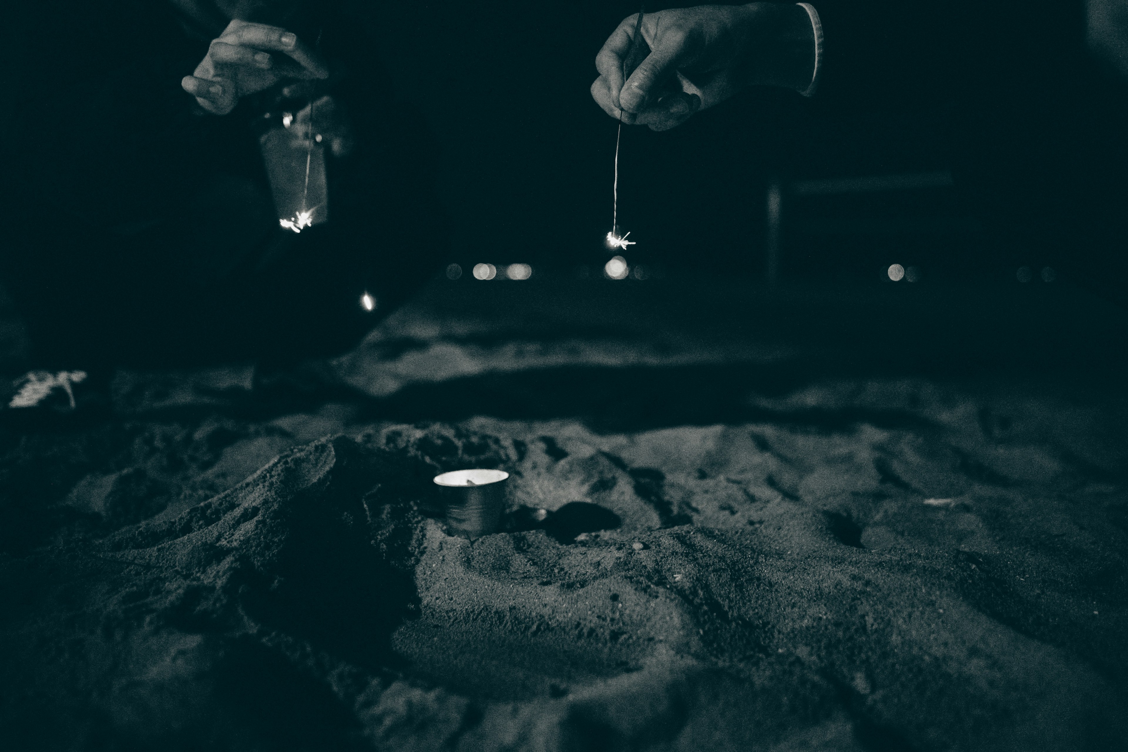 Scene of hands placing a candle on sand in a dark background