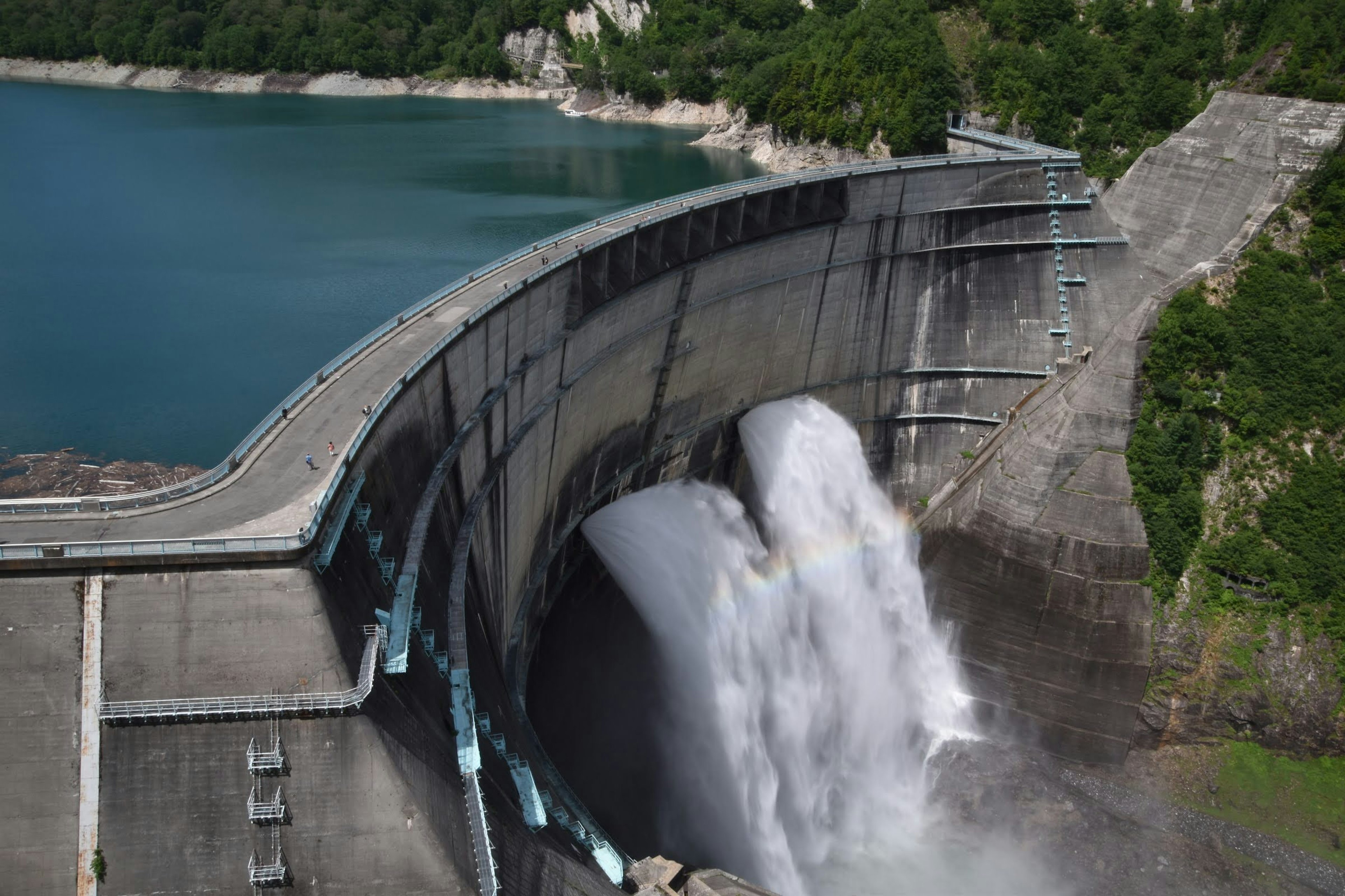 Water cascading from a dam into a reservoir surrounded by greenery