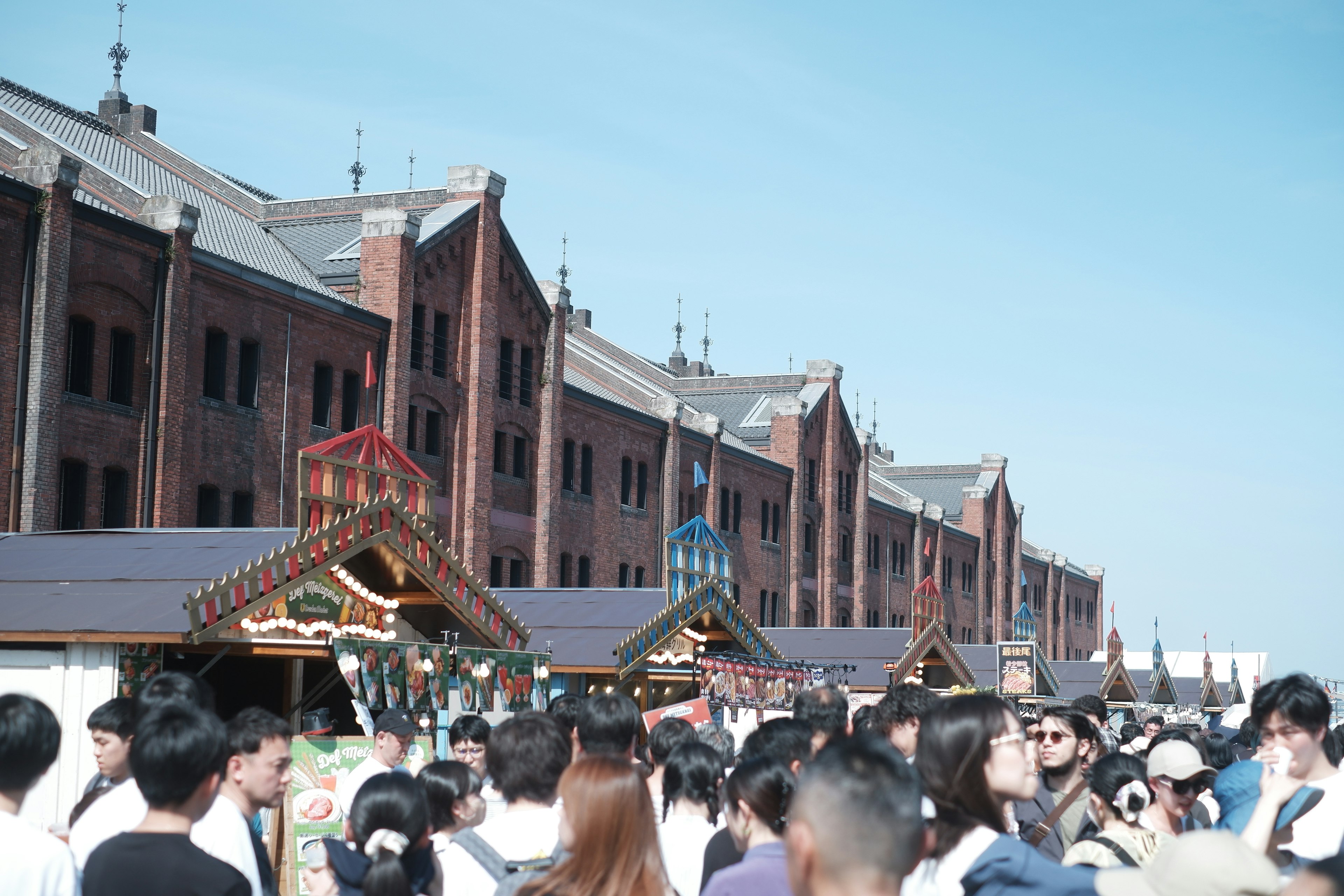 Menschenmenge auf einem Markt mit roten Backsteingebäuden im Hintergrund