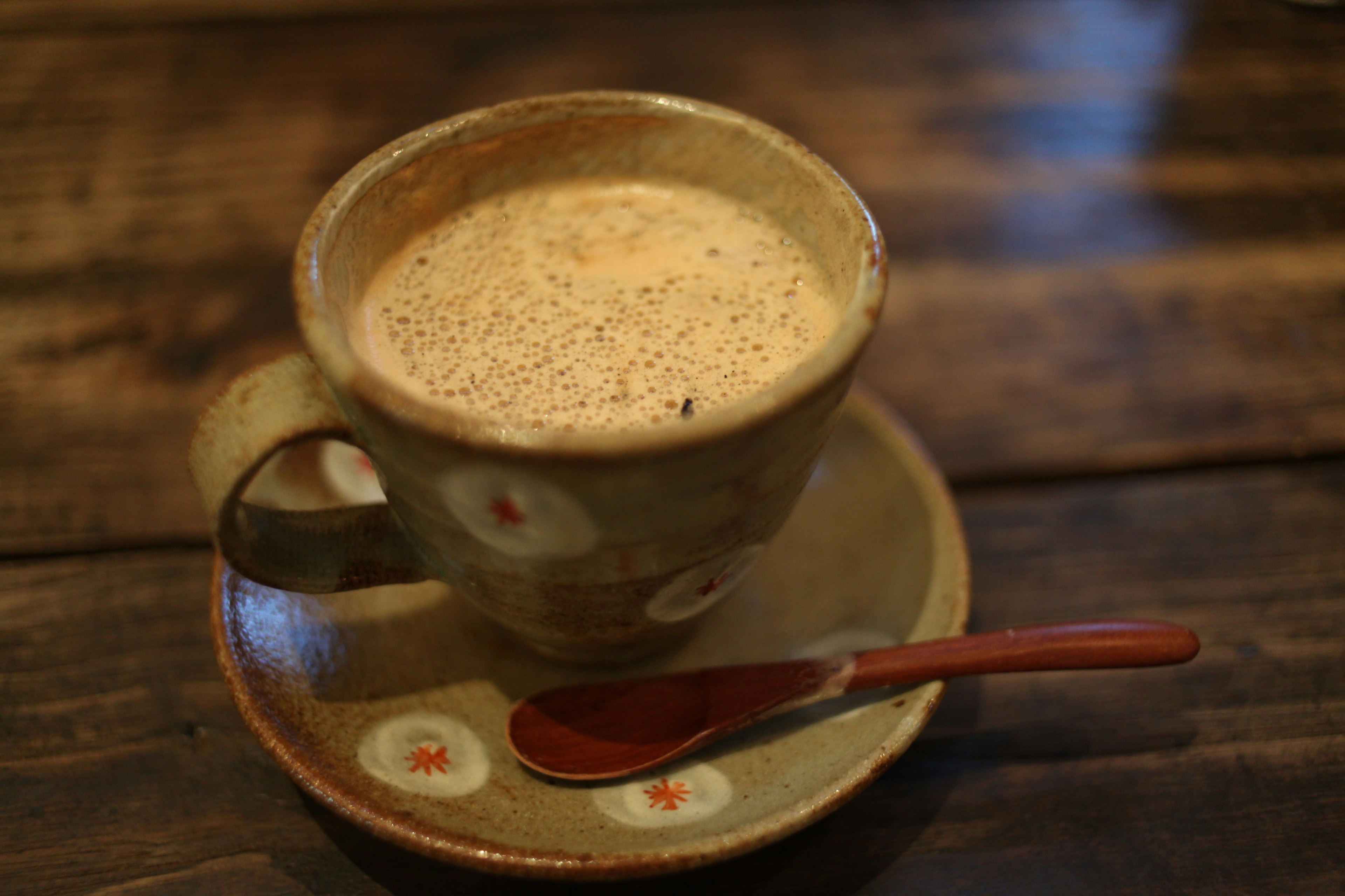 Ein schaumiges Getränk in einer braunen Keramiktasse mit einem kleinen Löffel auf einer Untertasse