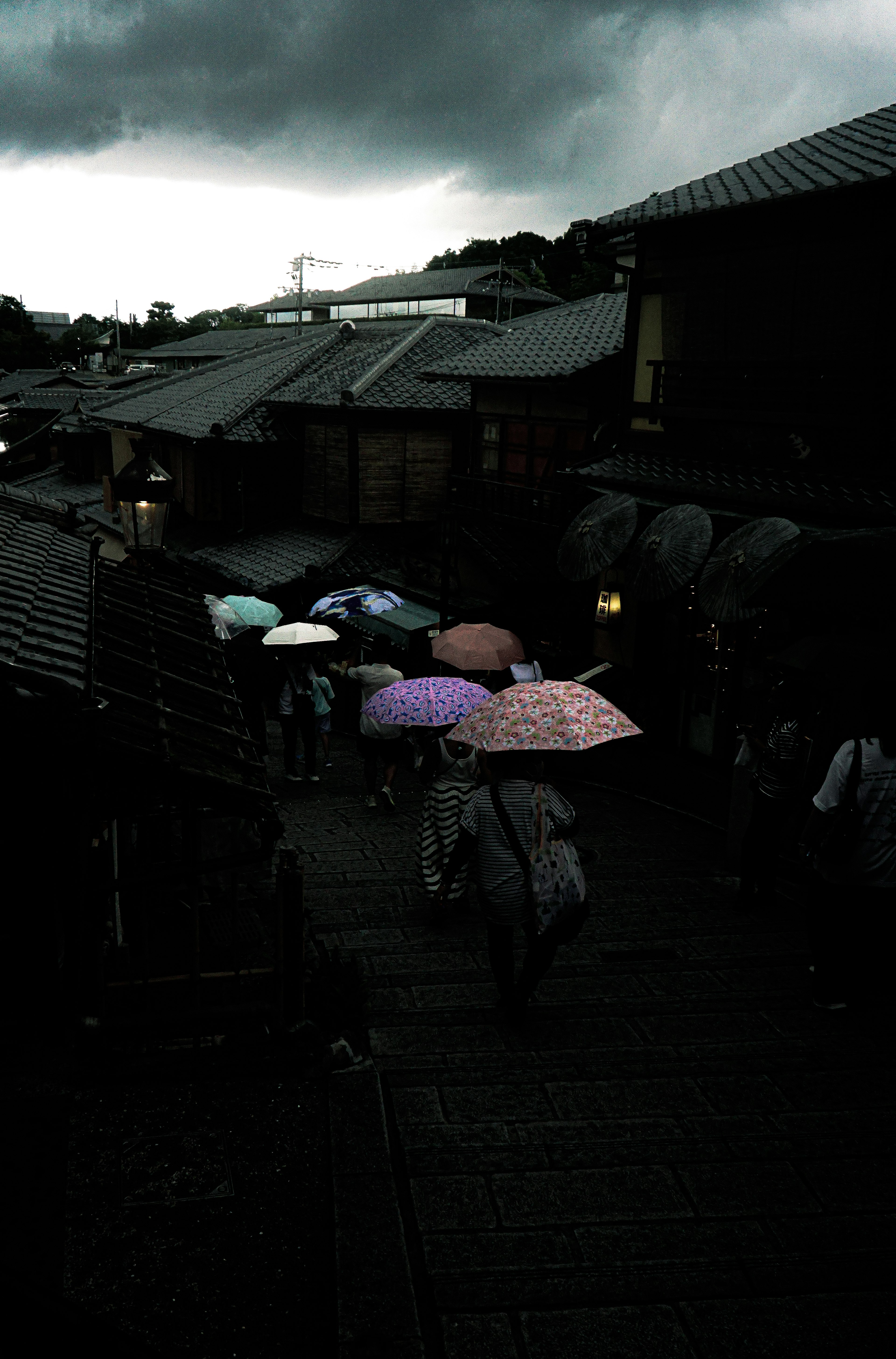 雨傘をさした人々が歩く薄暗い街並み