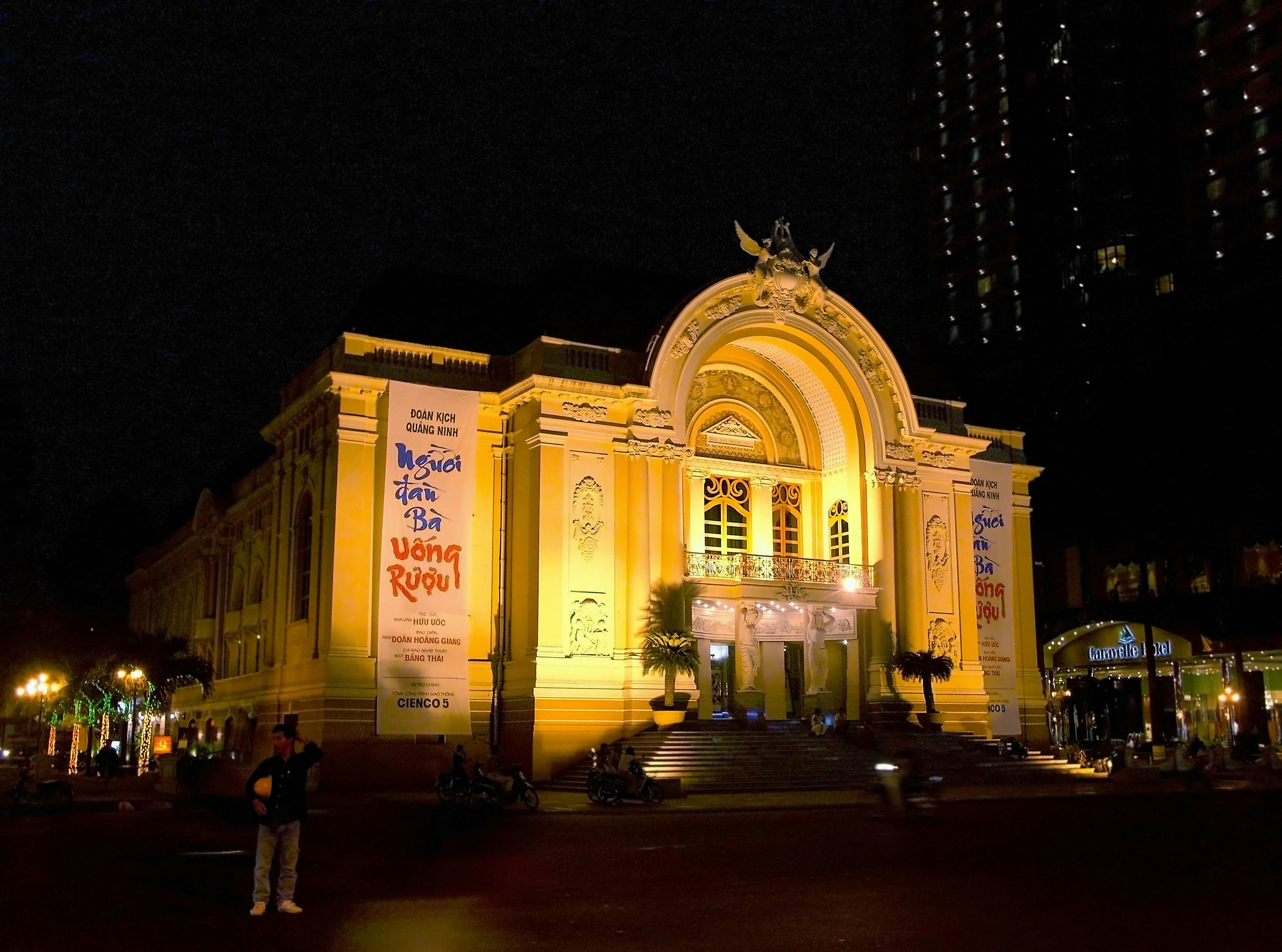 Facade of the opera house illuminated at night with people nearby