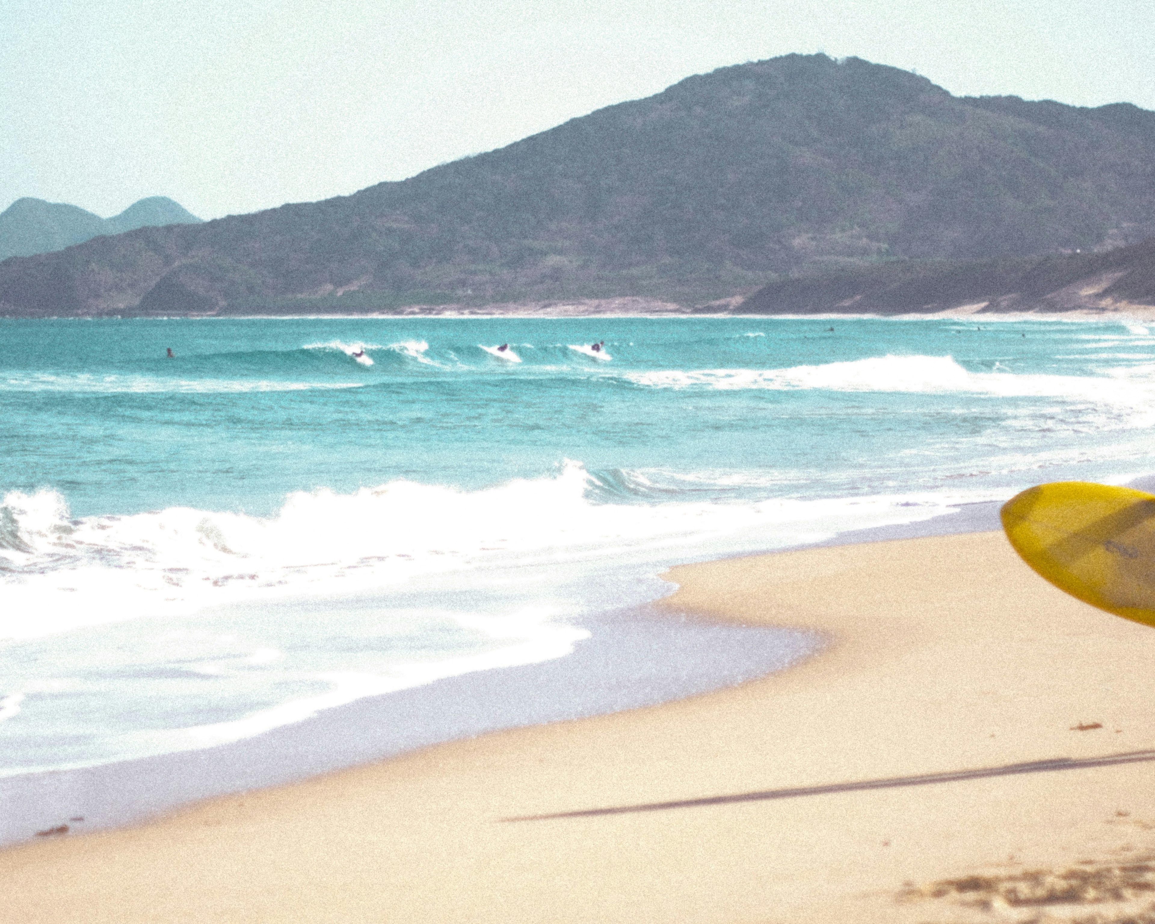 Pemandangan pantai dengan papan selancar kuning dan ombak lembut