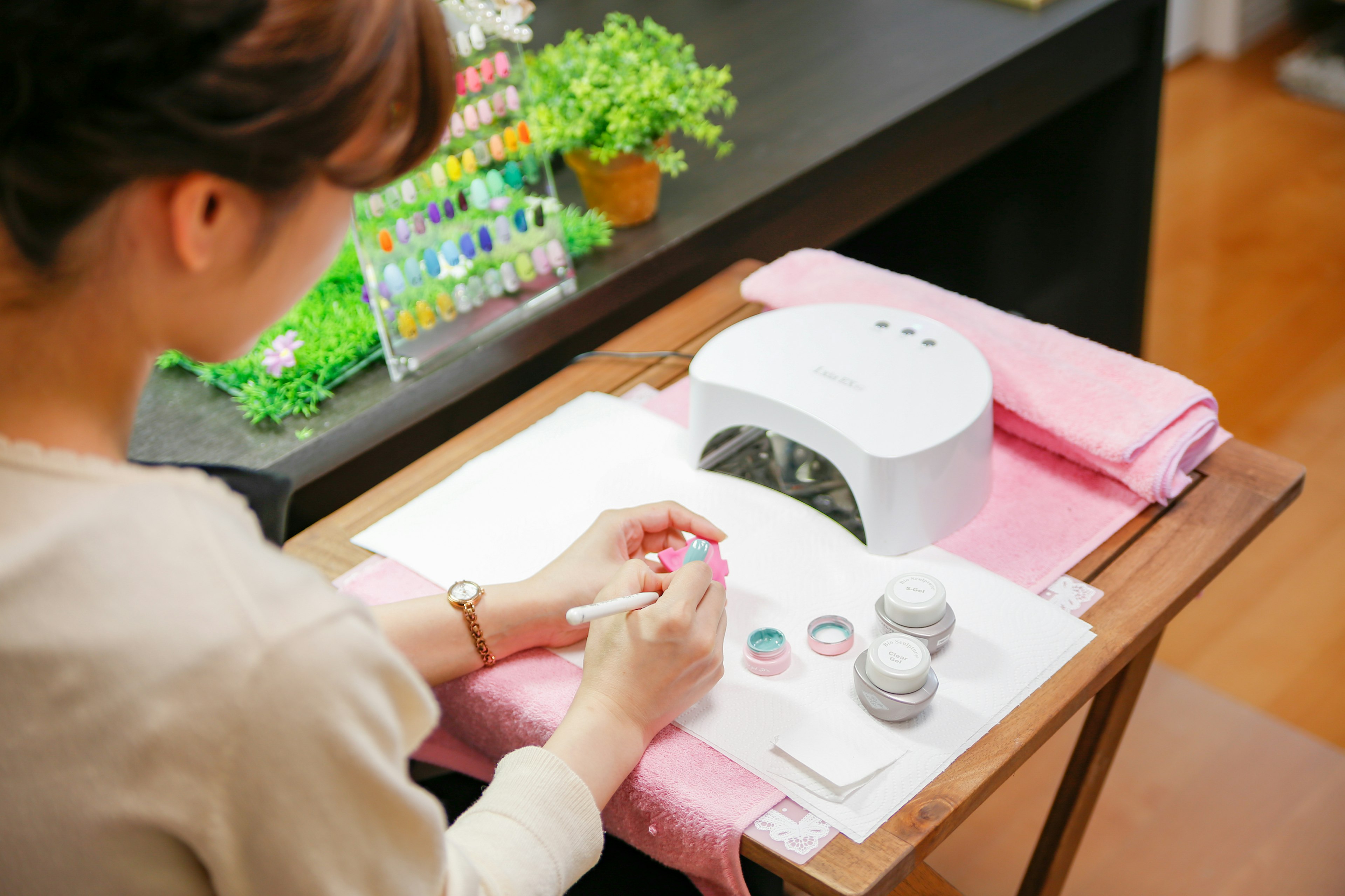 Mujer aplicando arte en uñas con una lámpara de uñas y esmaltes coloridos