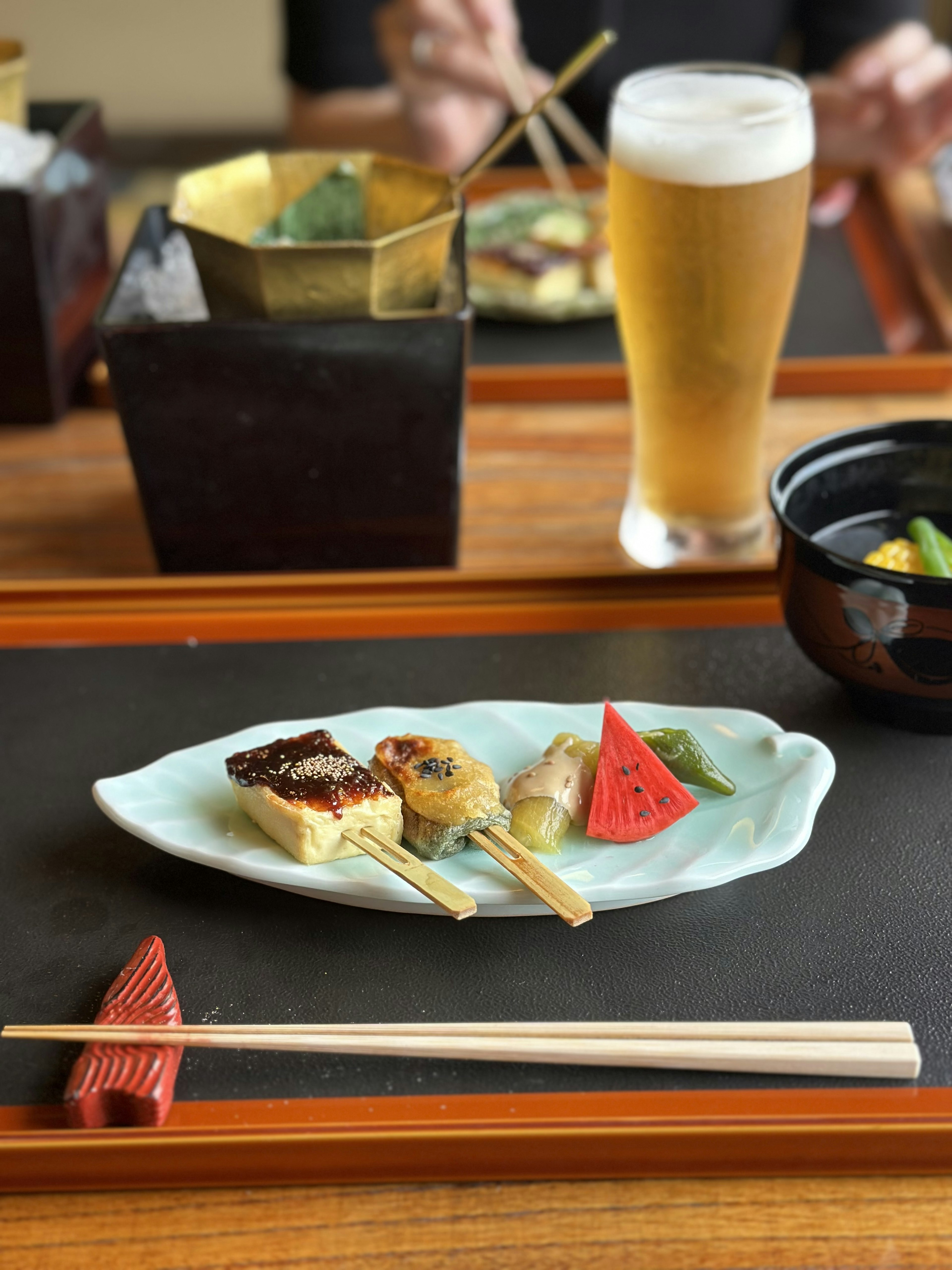 Une assiette de cuisine japonaise avec des brochettes grillées et des fruits rouges accompagnée d'une bière et de cornichons sur la table