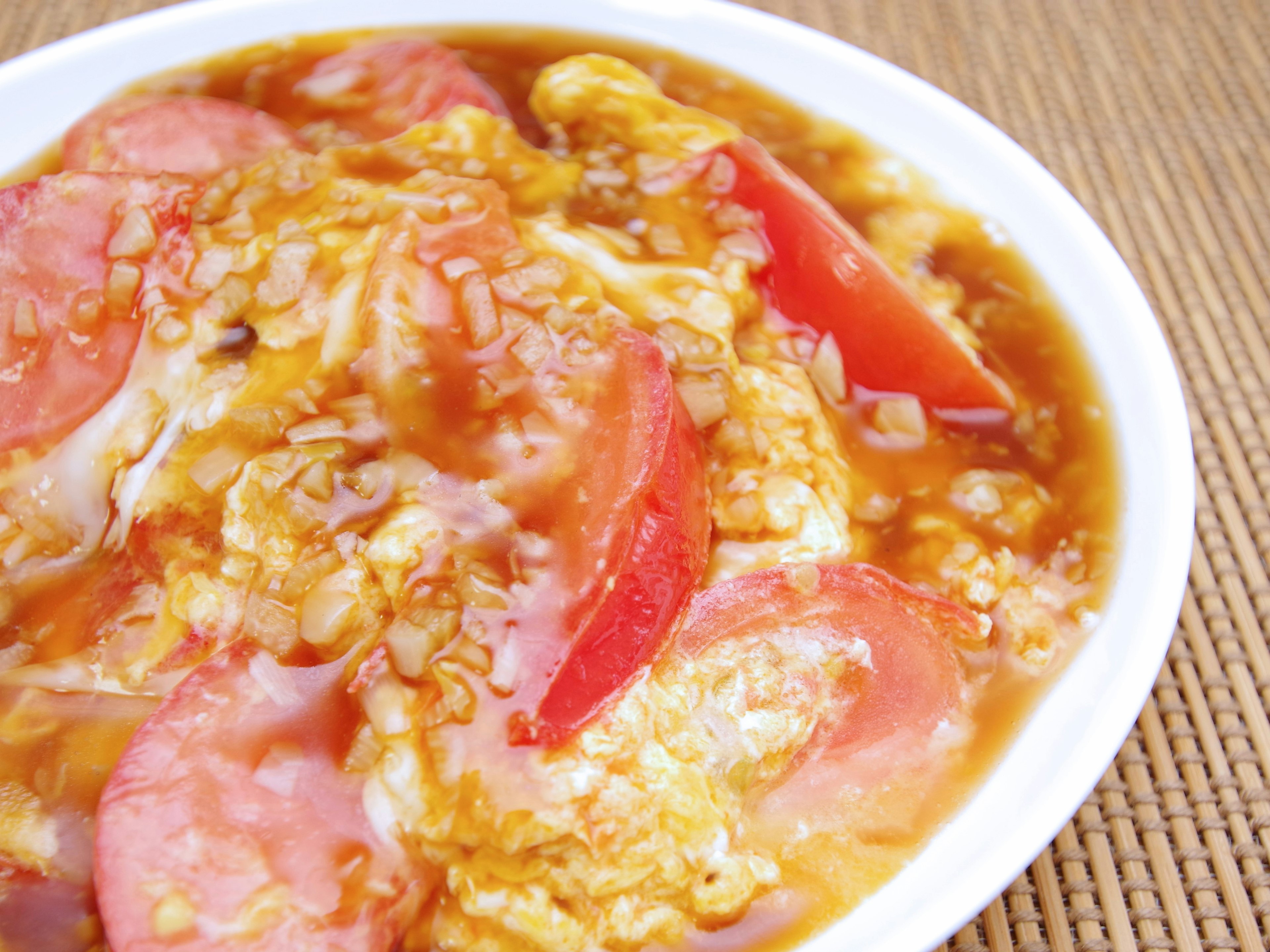 A dish of scrambled eggs with tomatoes and sausages served in a white bowl