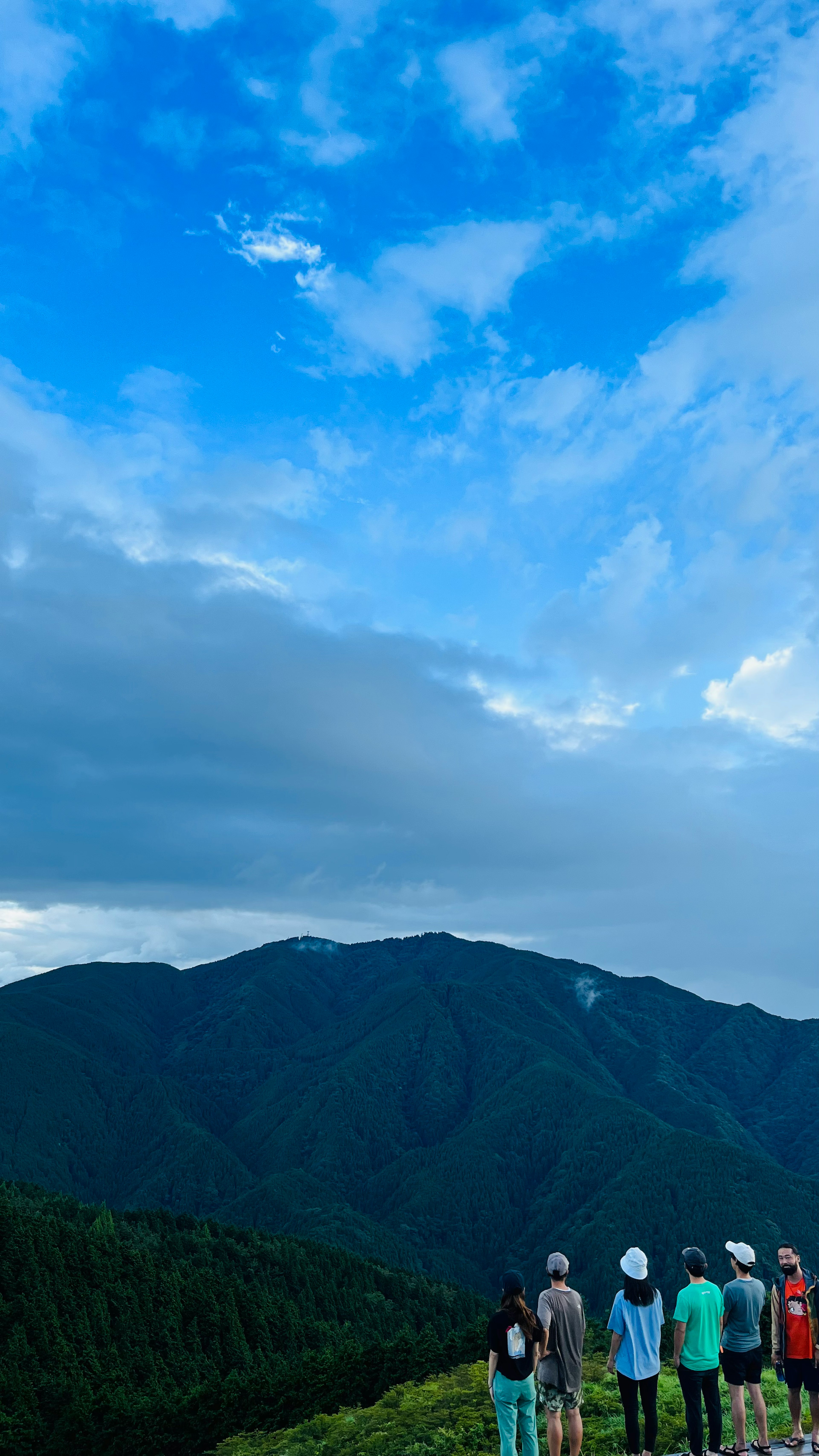 青空と雲の下で山を見つめる人々の集団