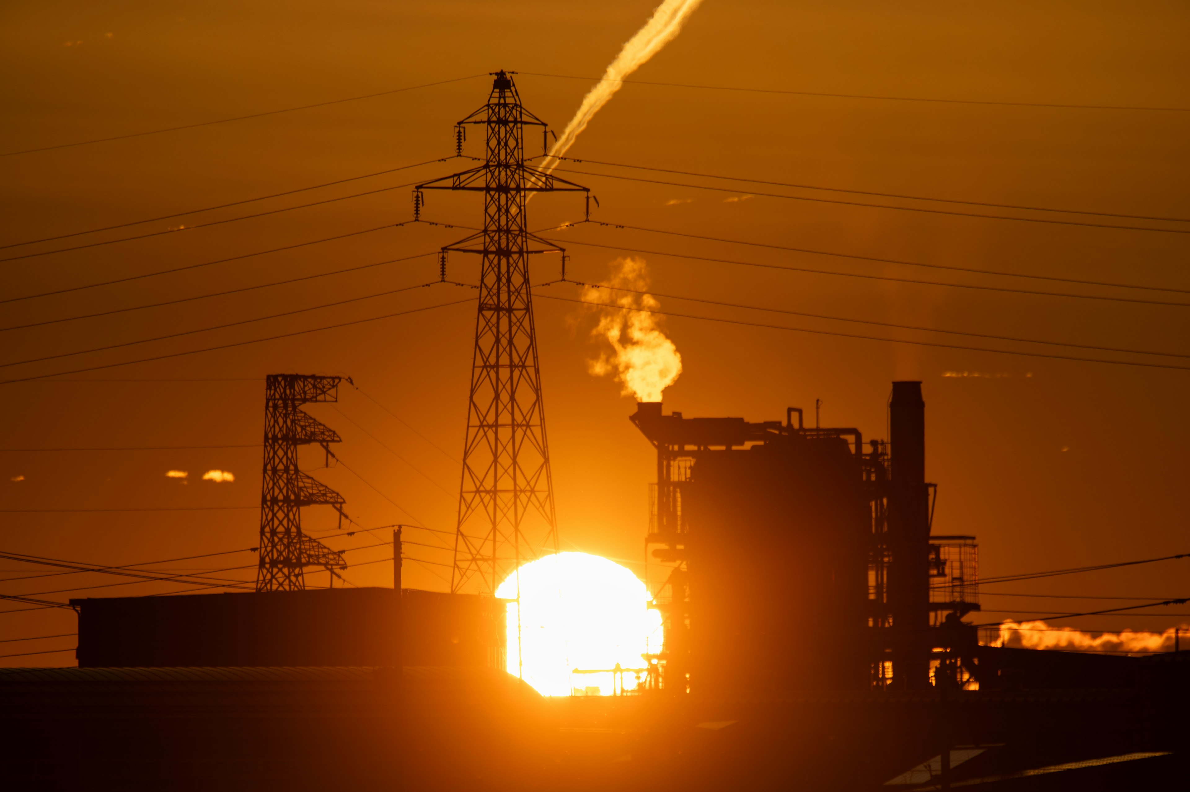 Puesta de sol detrás de estructuras industriales con humo y líneas eléctricas