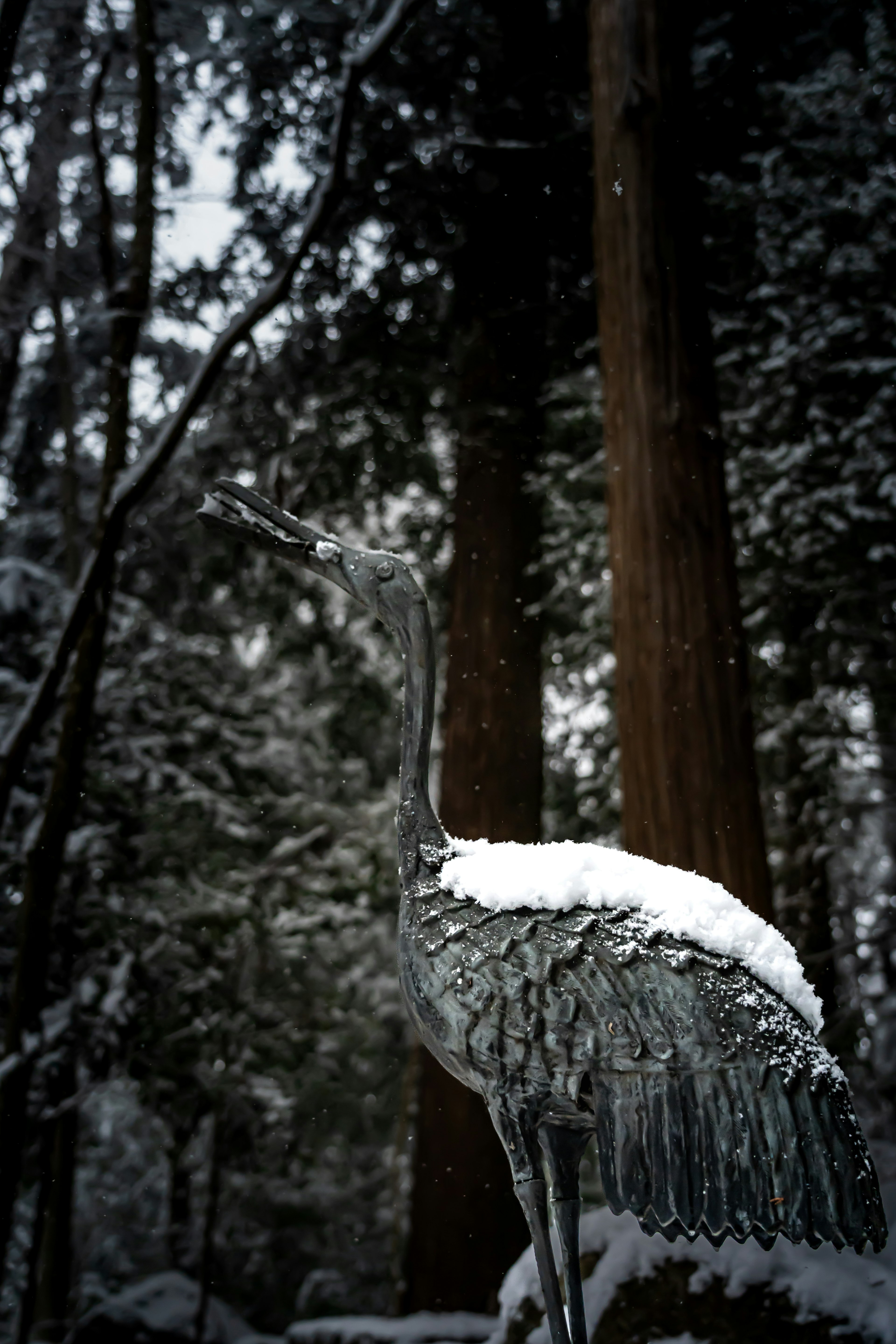 Une statue de grue couverte de neige se dresse dans une forêt enneigée