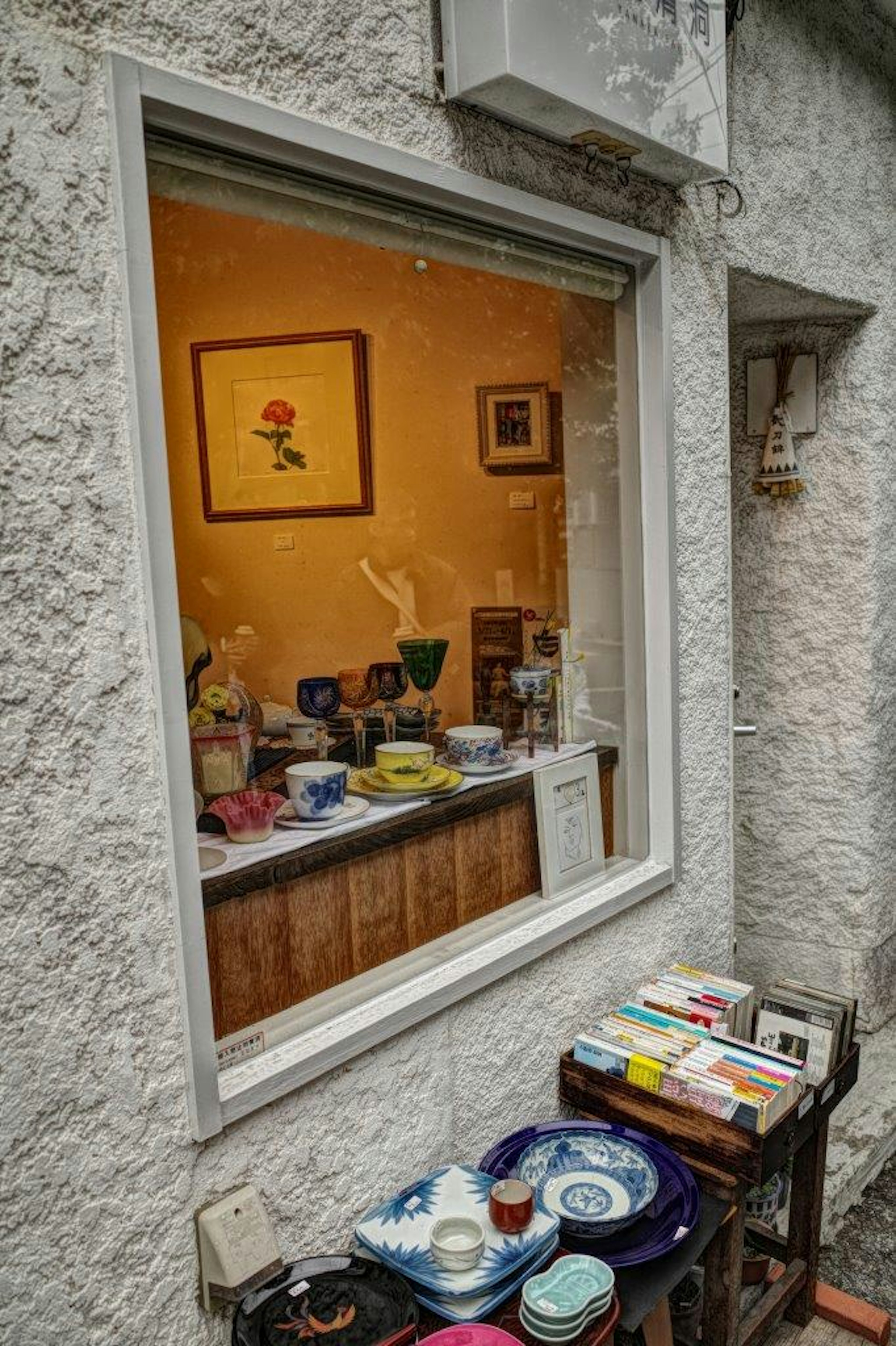 Warmly colored room visible through a window featuring a flower painting and various colorful dishes and items