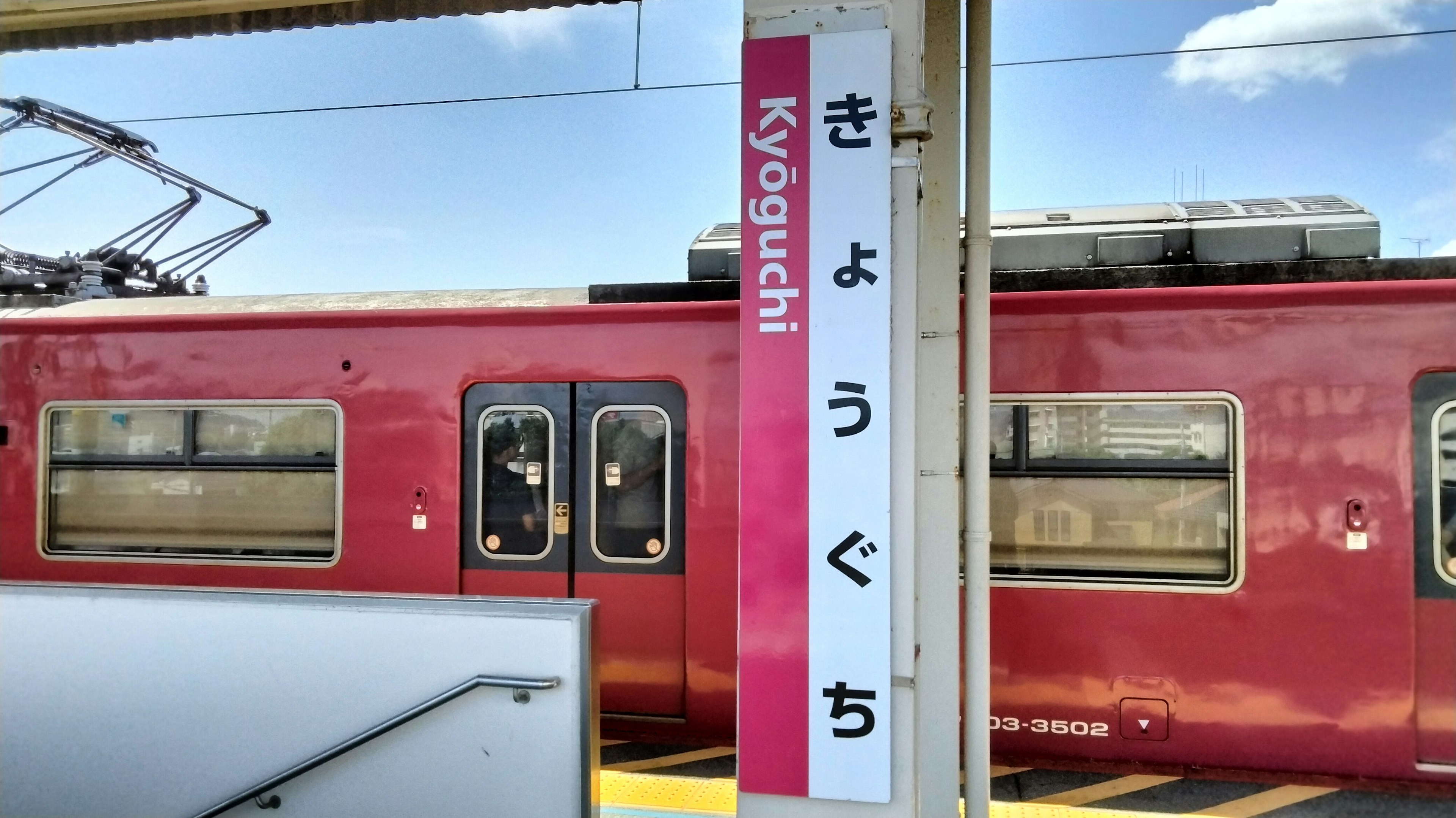 赤い電車と駅名看板が見える駅の風景