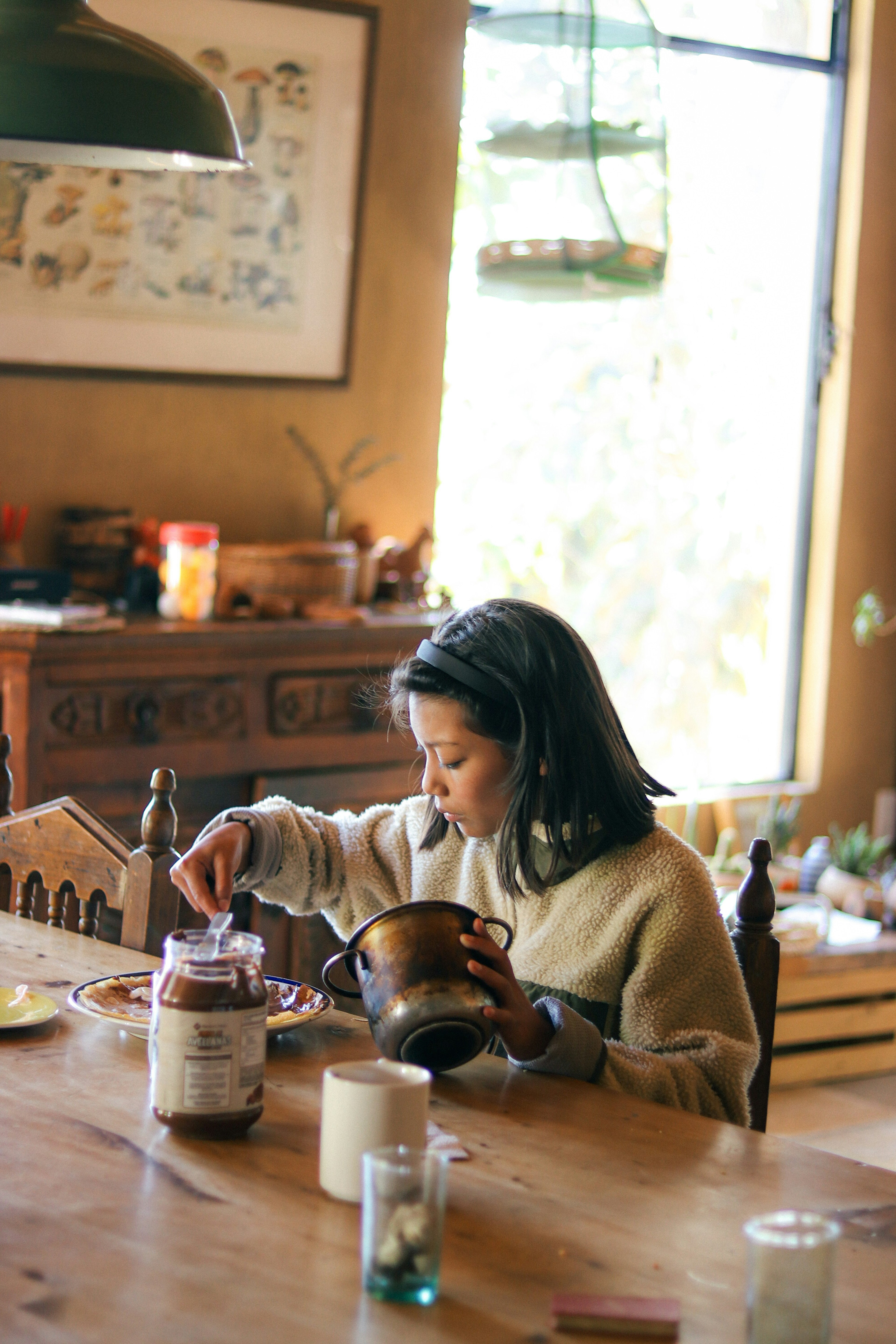 Child spooning jam into a jar at a wooden table