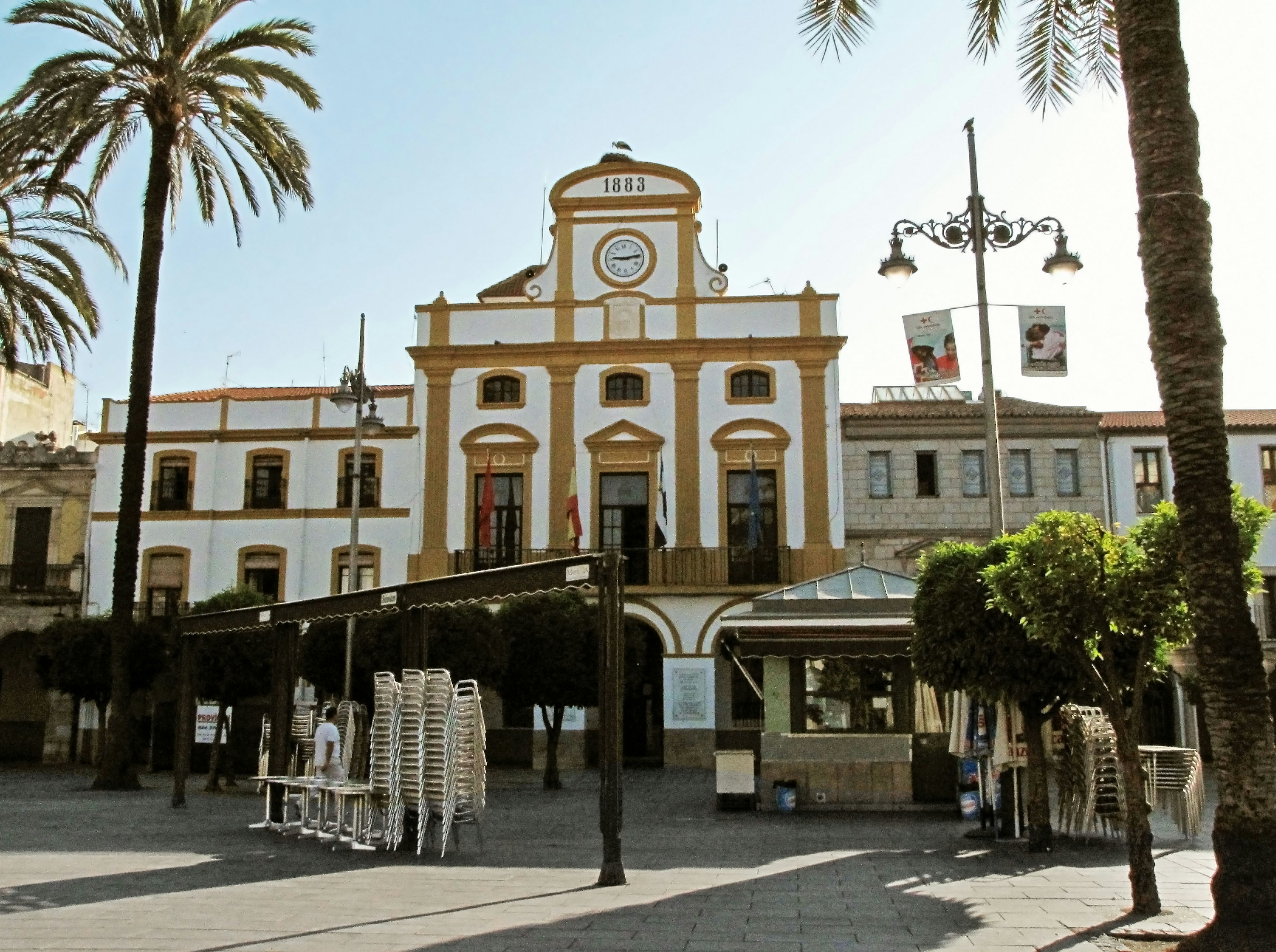 Piazza con un edificio bianco con dettagli arancioni e palme