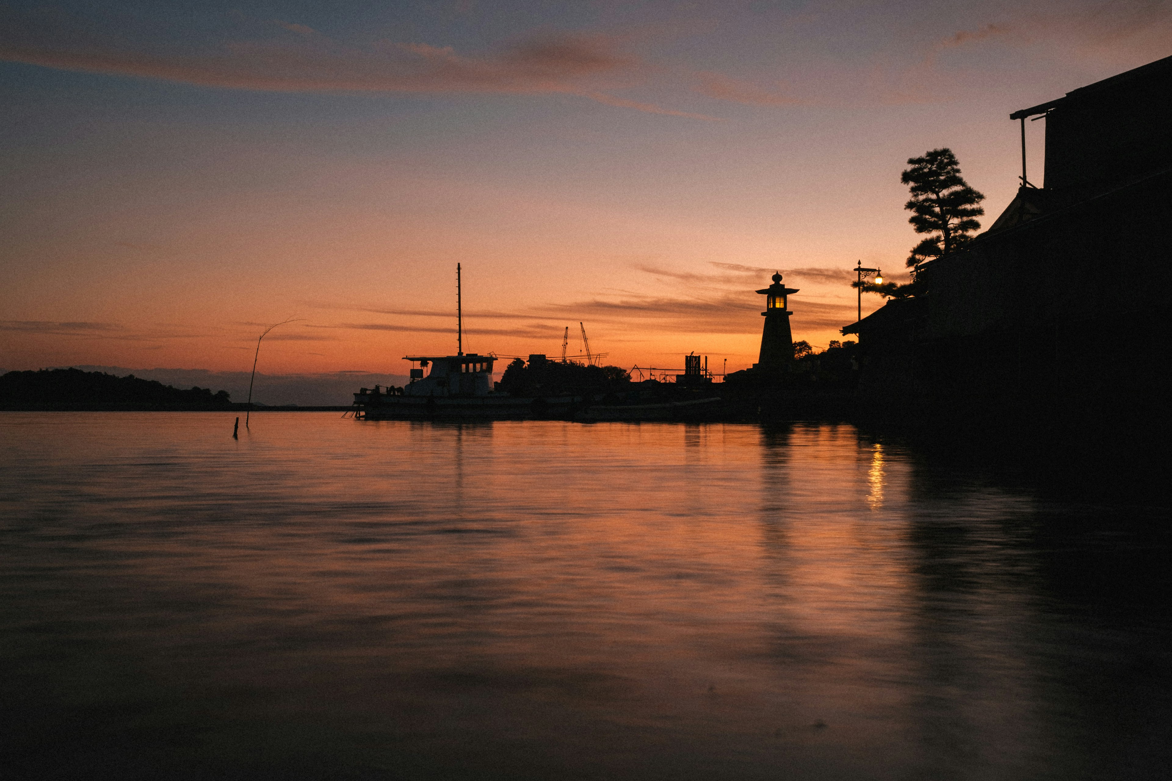 Pemandangan laut dengan mercusuar dan air tenang saat matahari terbenam