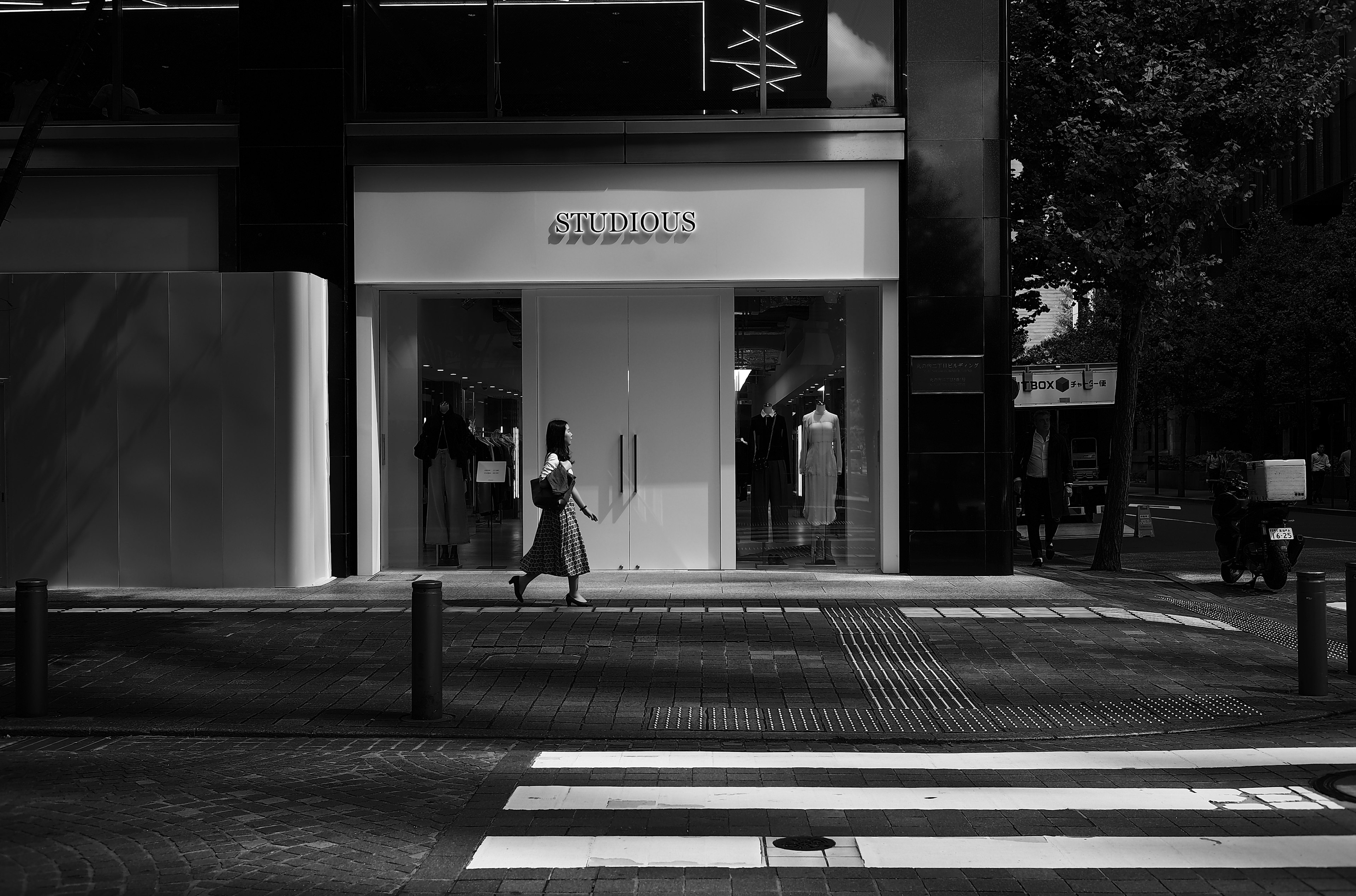 Une femme marchant dans une scène de rue en noir et blanc devant un magasin