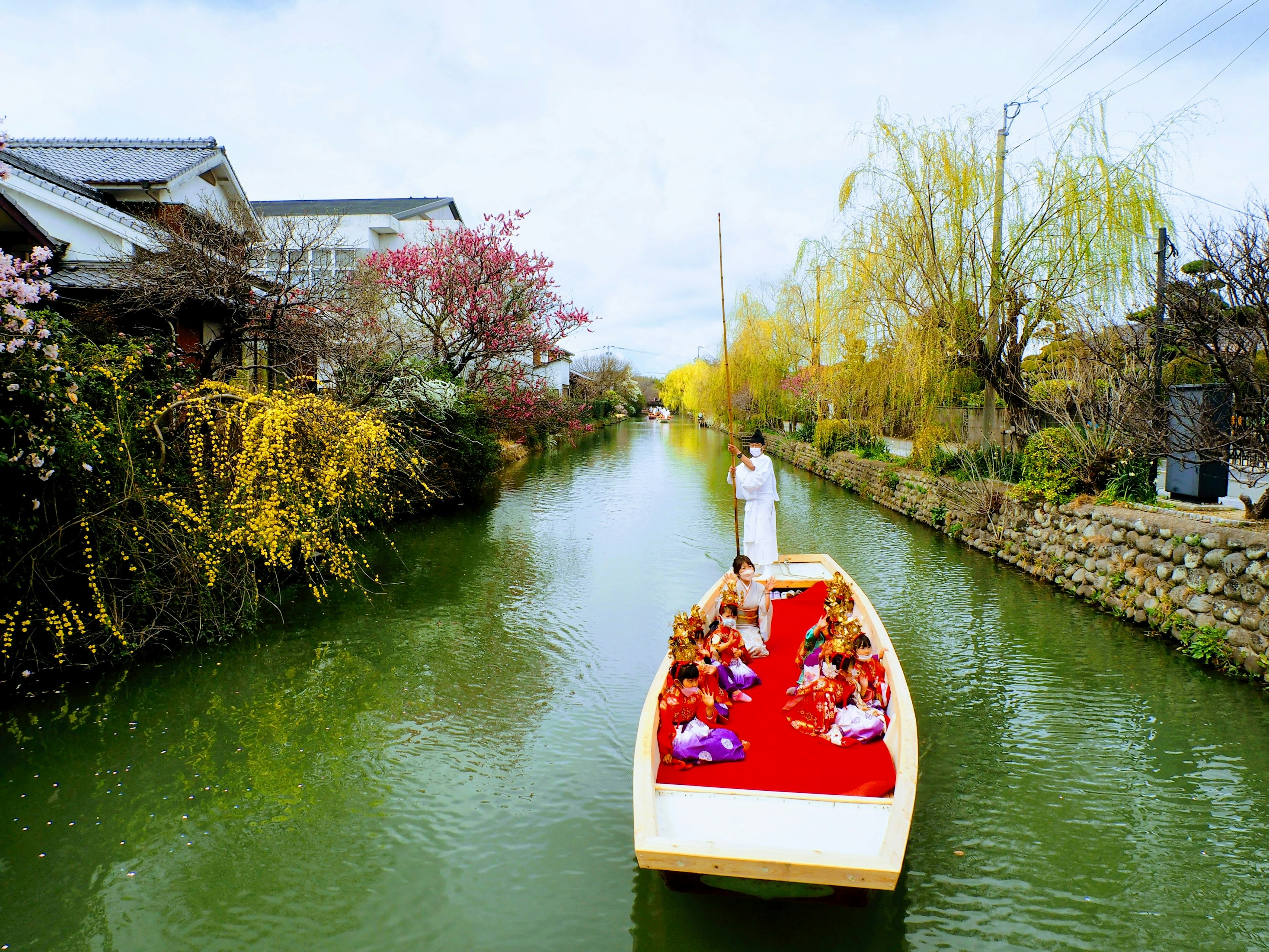 Ein Boot mit Menschen in bunten Kleidern, das durch einen grünen Kanal mit blühenden Blumen gleitet