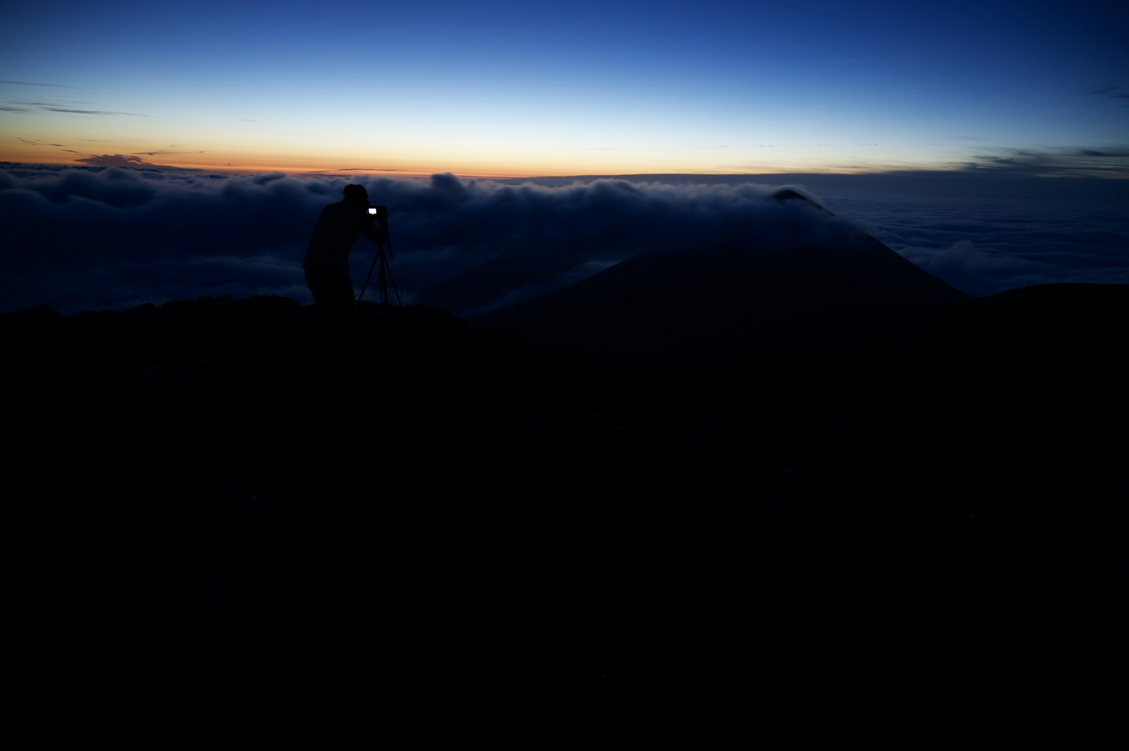 山の頂上でカメラを持つ登山者のシルエットと美しい朝焼け