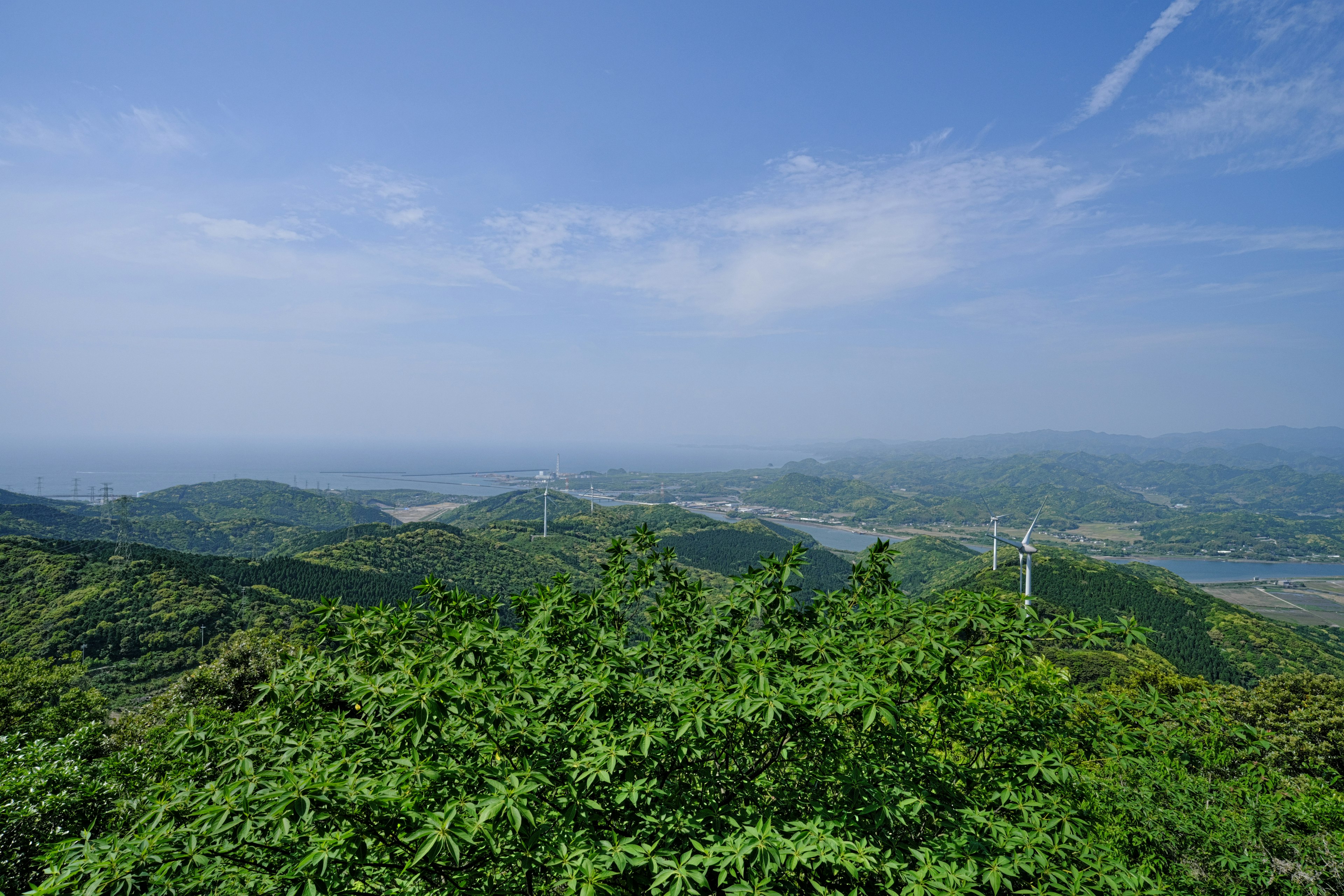 郁郁蔥蔥的綠色山脈和晴朗的藍天，遠處可見風力發電機