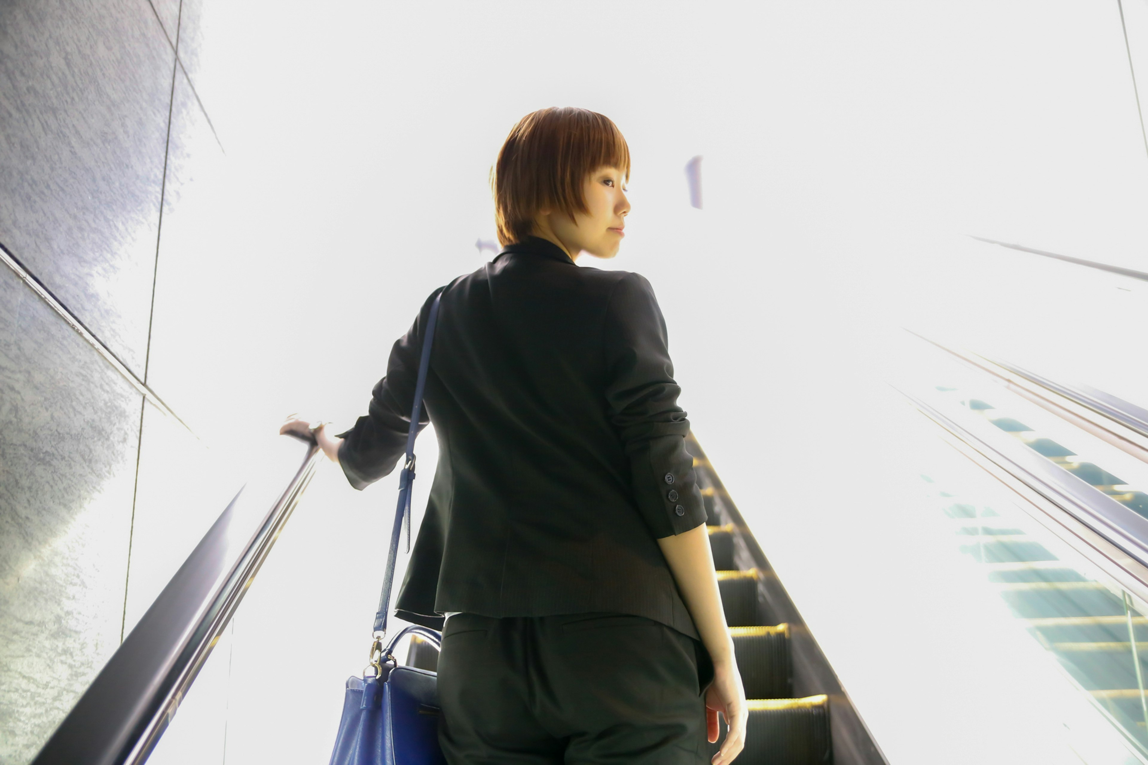 Woman ascending an escalator towards bright light