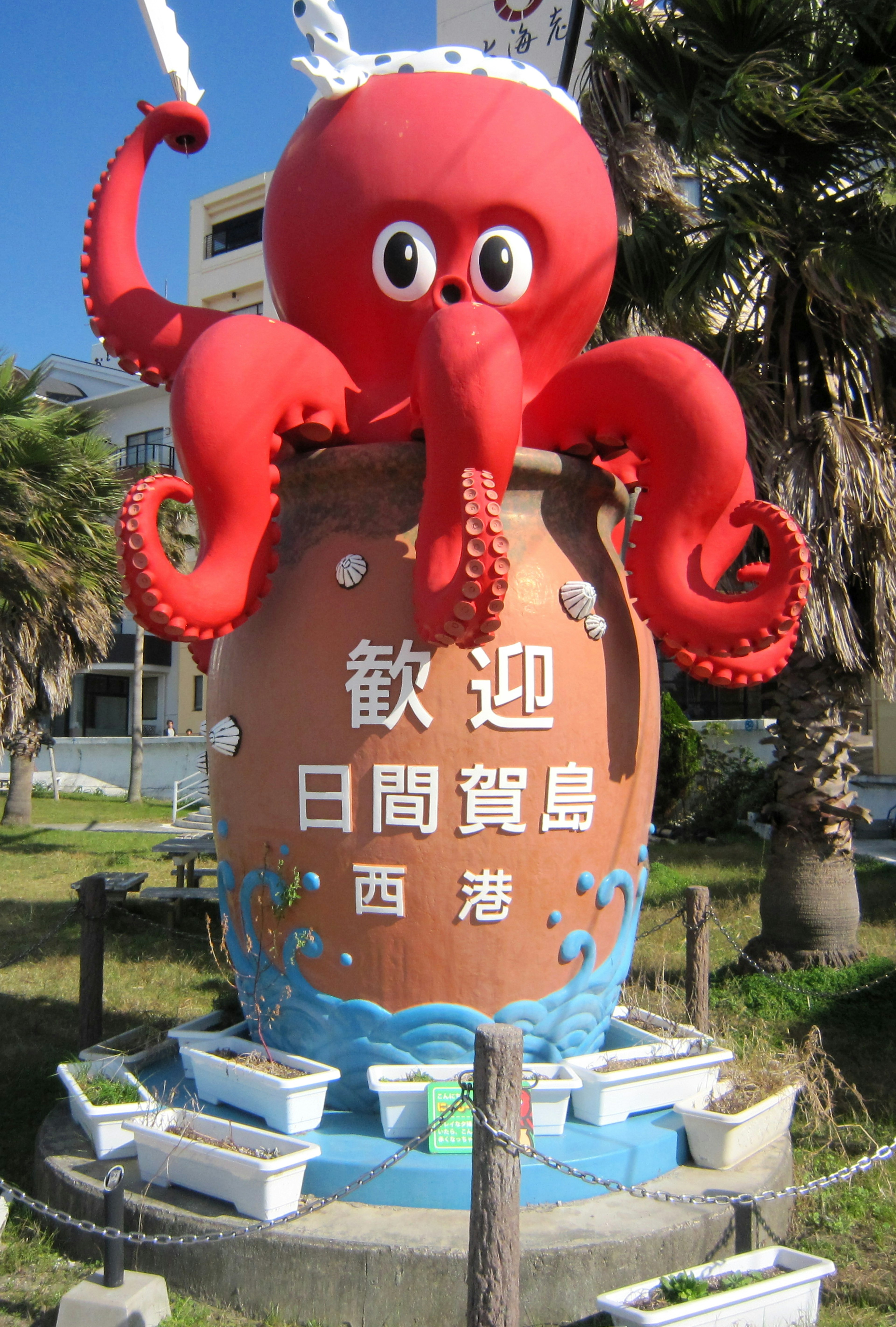 A red octopus statue sitting atop a pot with a welcome sign