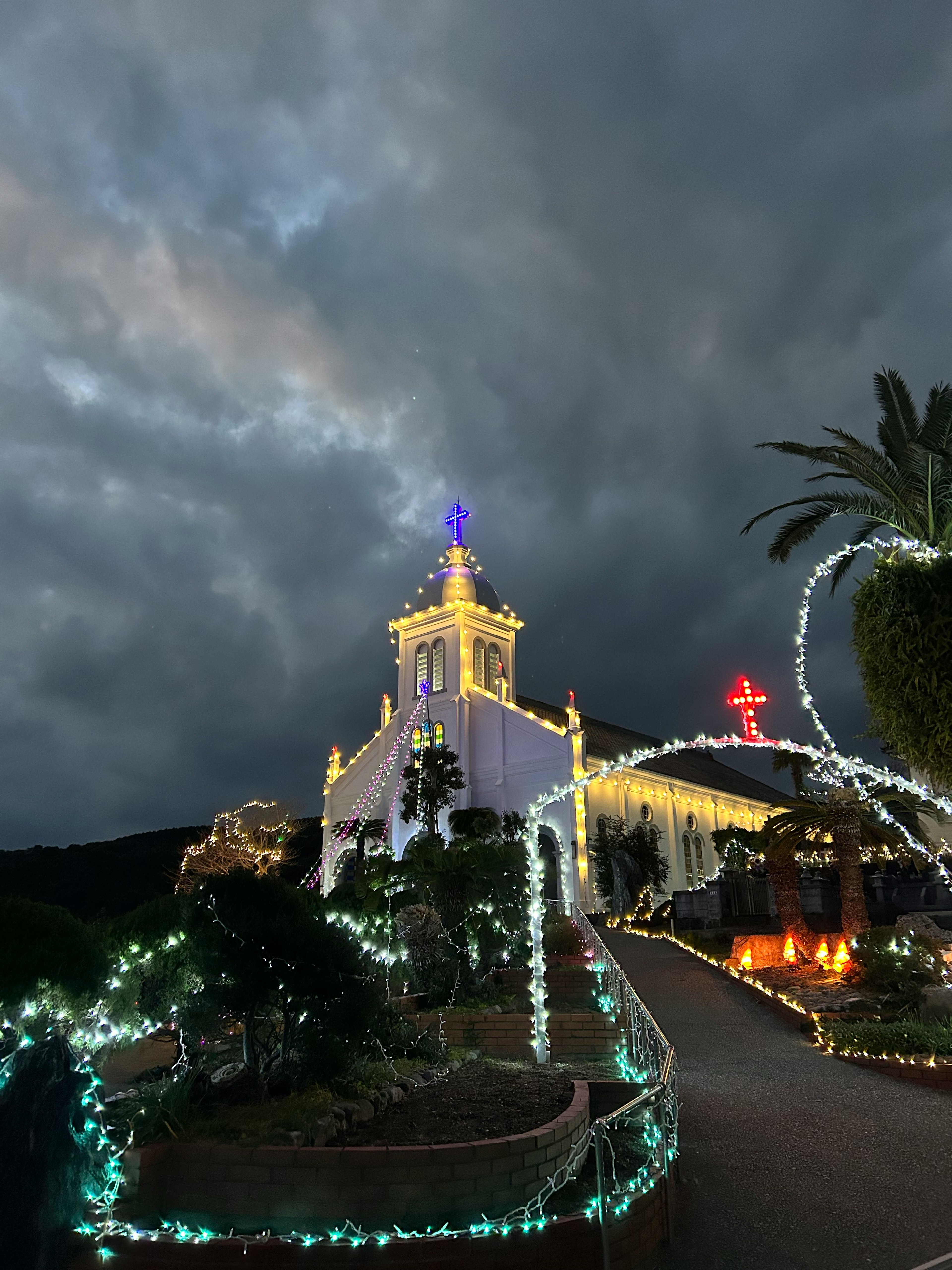 Kirche bei Nacht unter dramatischen Wolken mit Palmen beleuchtet