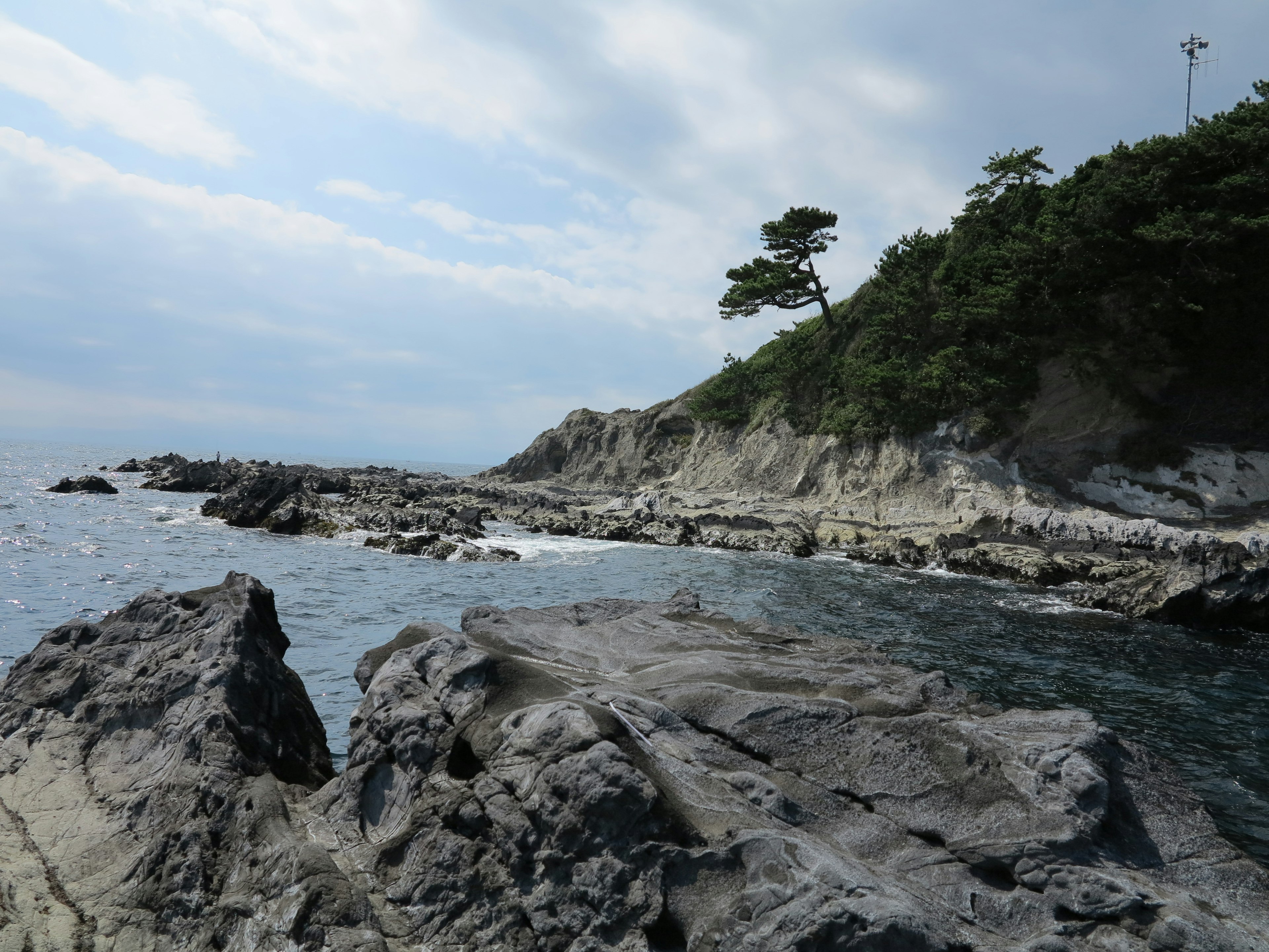 Paesaggio costiero roccioso con mare blu e cielo nuvoloso