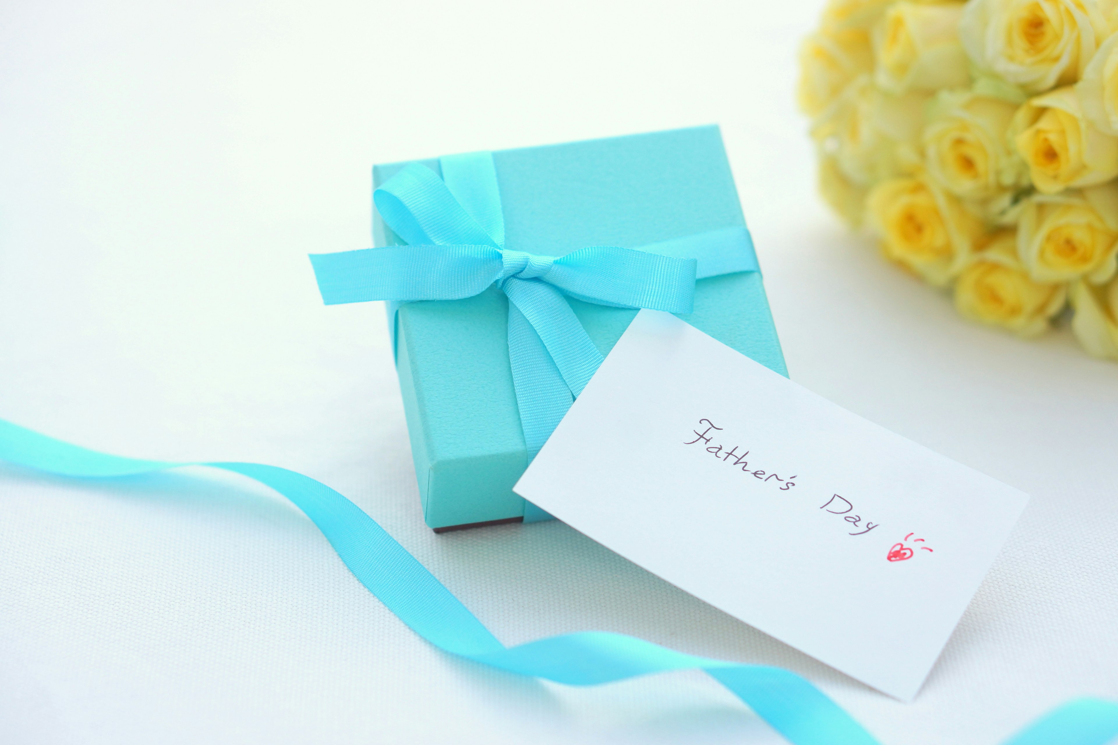 A blue gift box with a white card and a bouquet of yellow roses