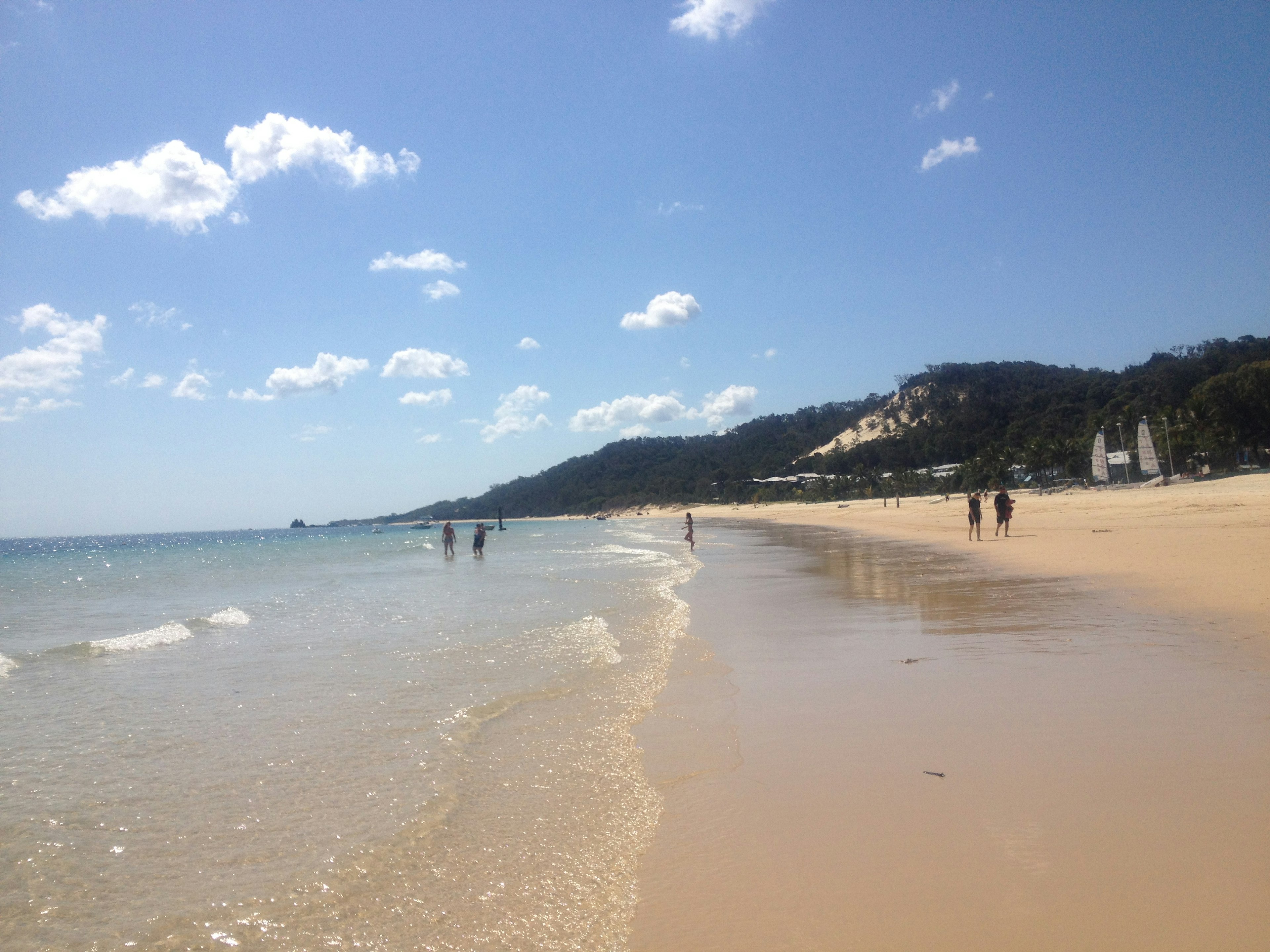 ฉากชายหาดท้องฟ้าสีฟ้าและทะเลสงบผู้คนเดินตามชายฝั่ง