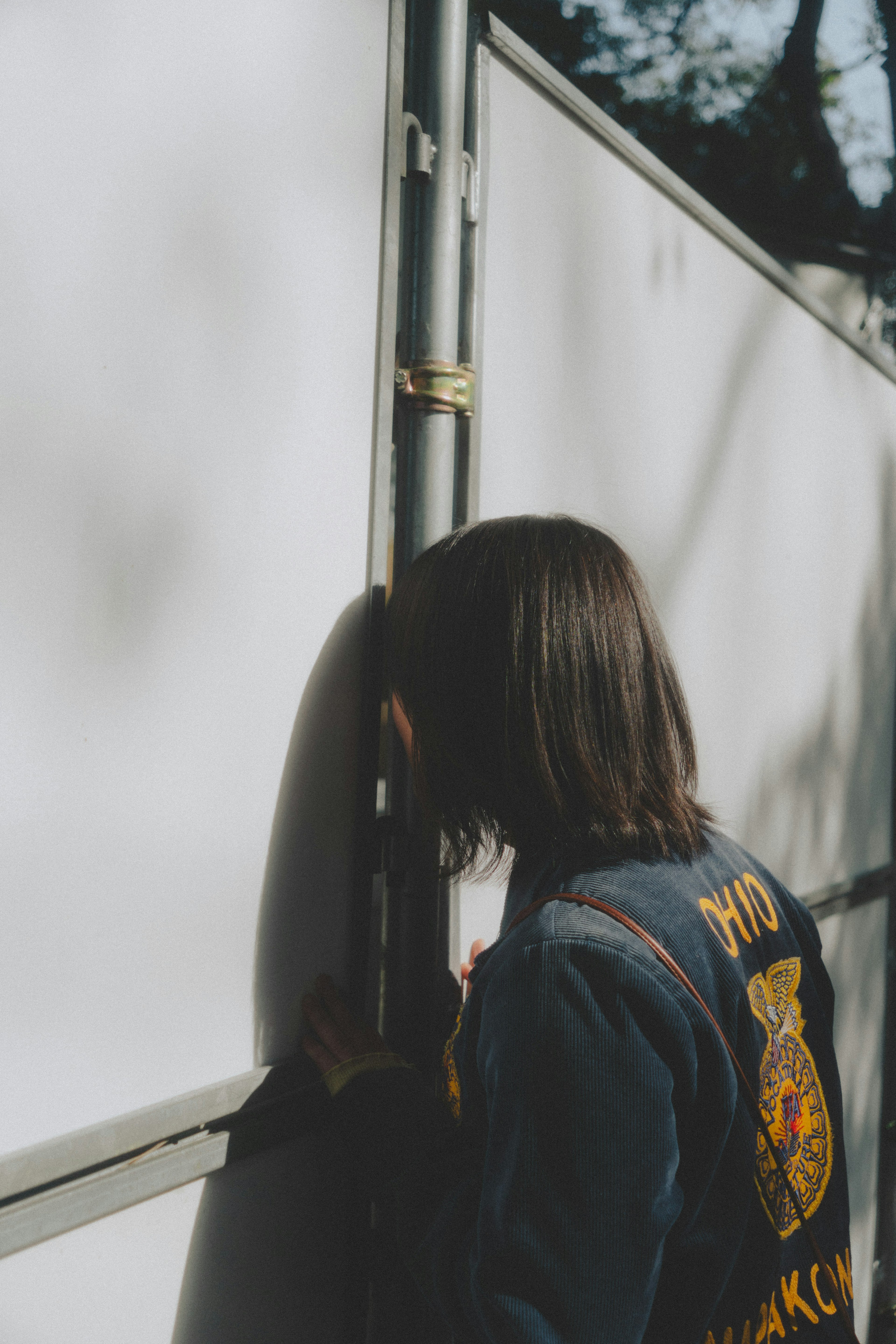 Femme s'appuyant contre un mur blanc avec une patch sur sa veste