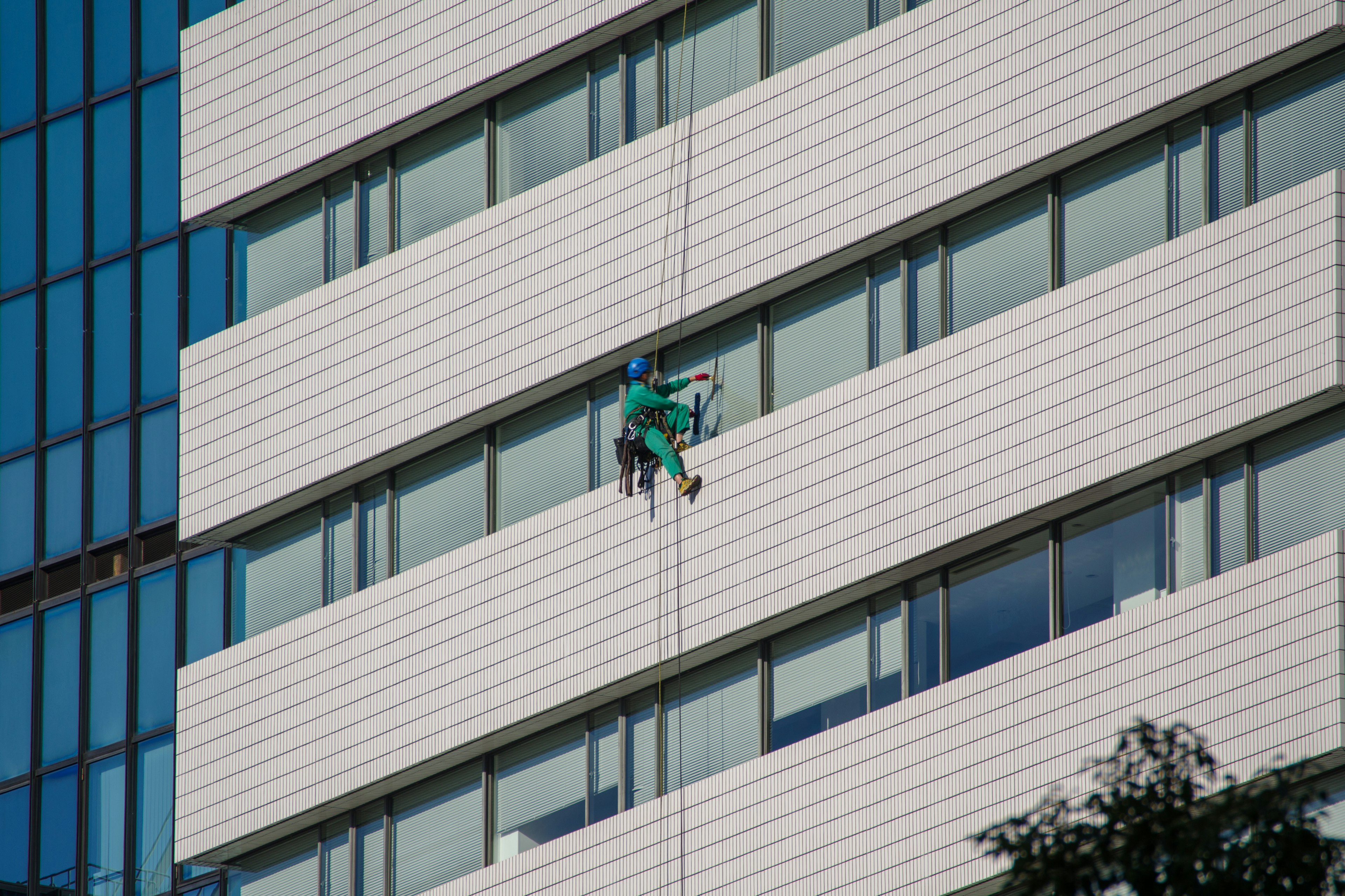 Arbeiter in grüner Kleidung reinigt Fenster eines Hochhauses