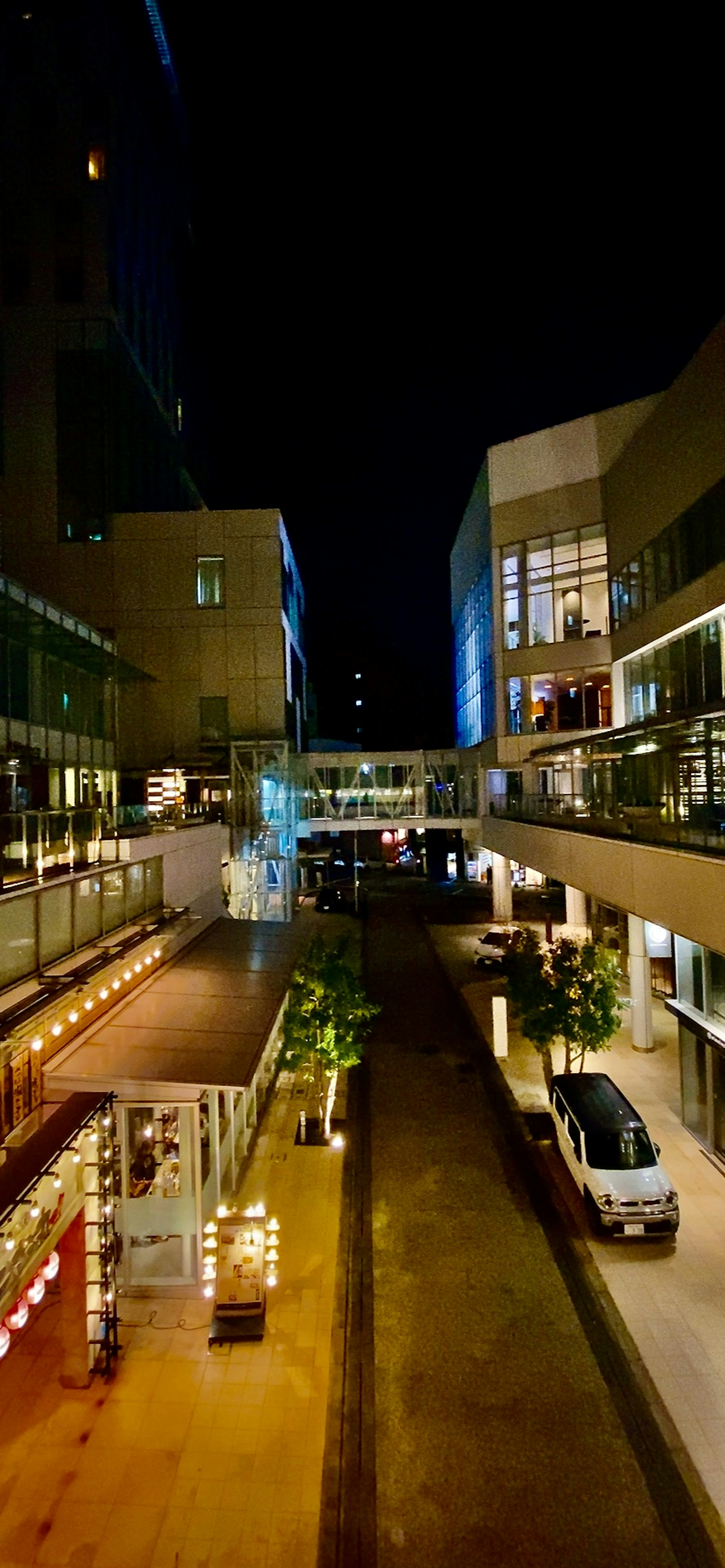 Shopping mall corridor at night with shops and cars