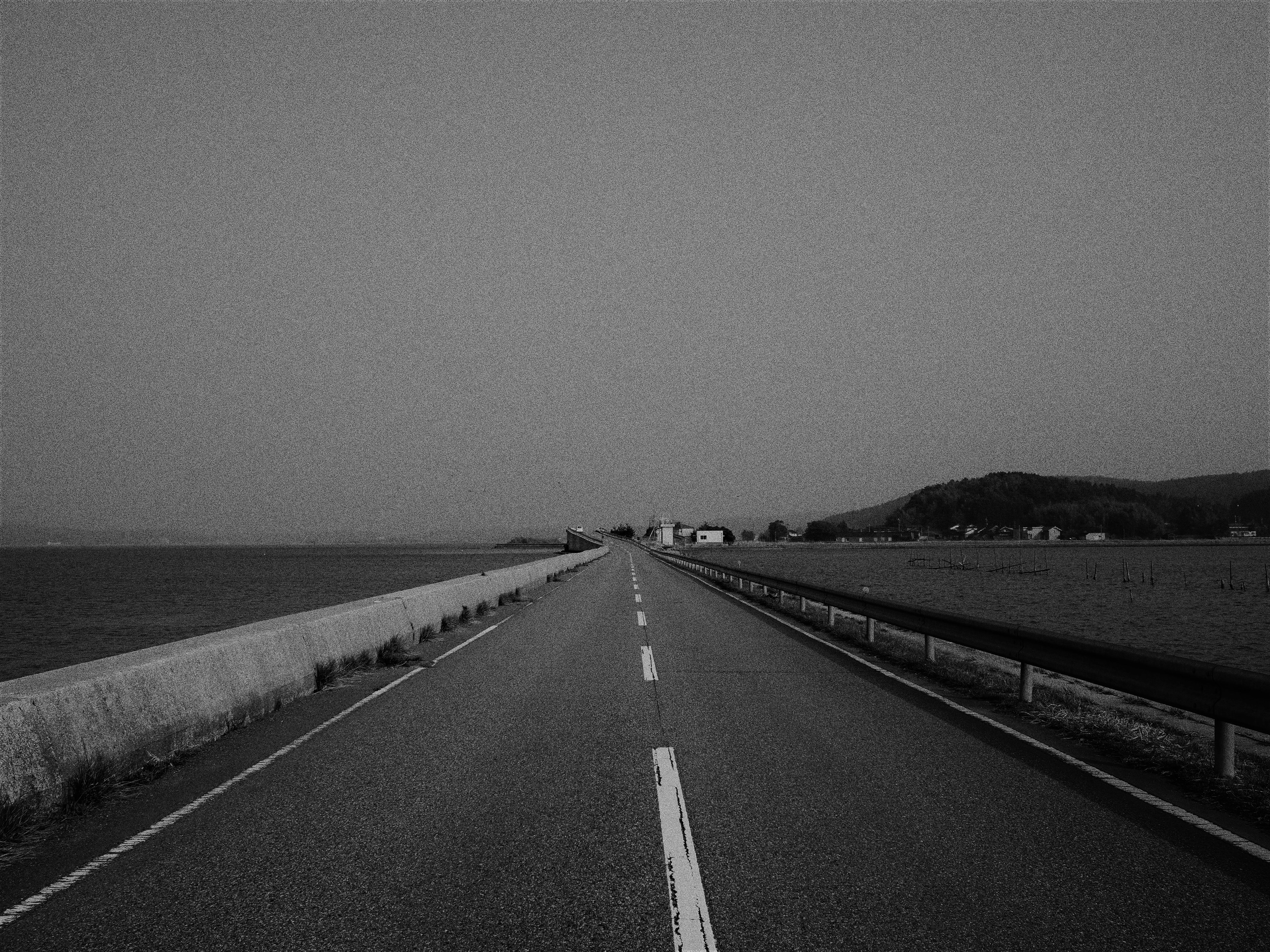 Black and white photo of a road alongside the sea Straight road with concrete guardrail