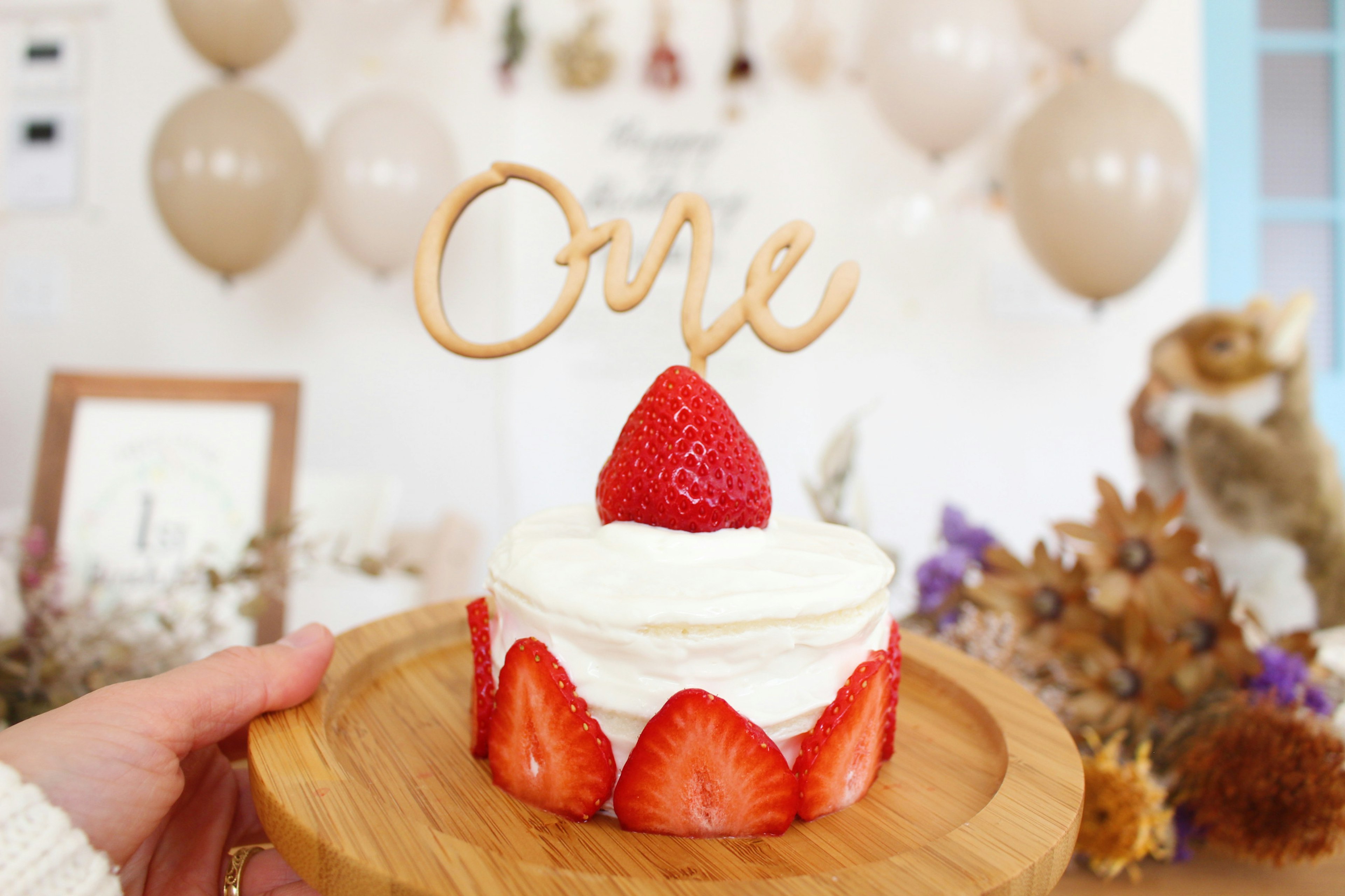 Un pequeño pastel cubierto de crema y fresas con un adorno de madera que dice Uno