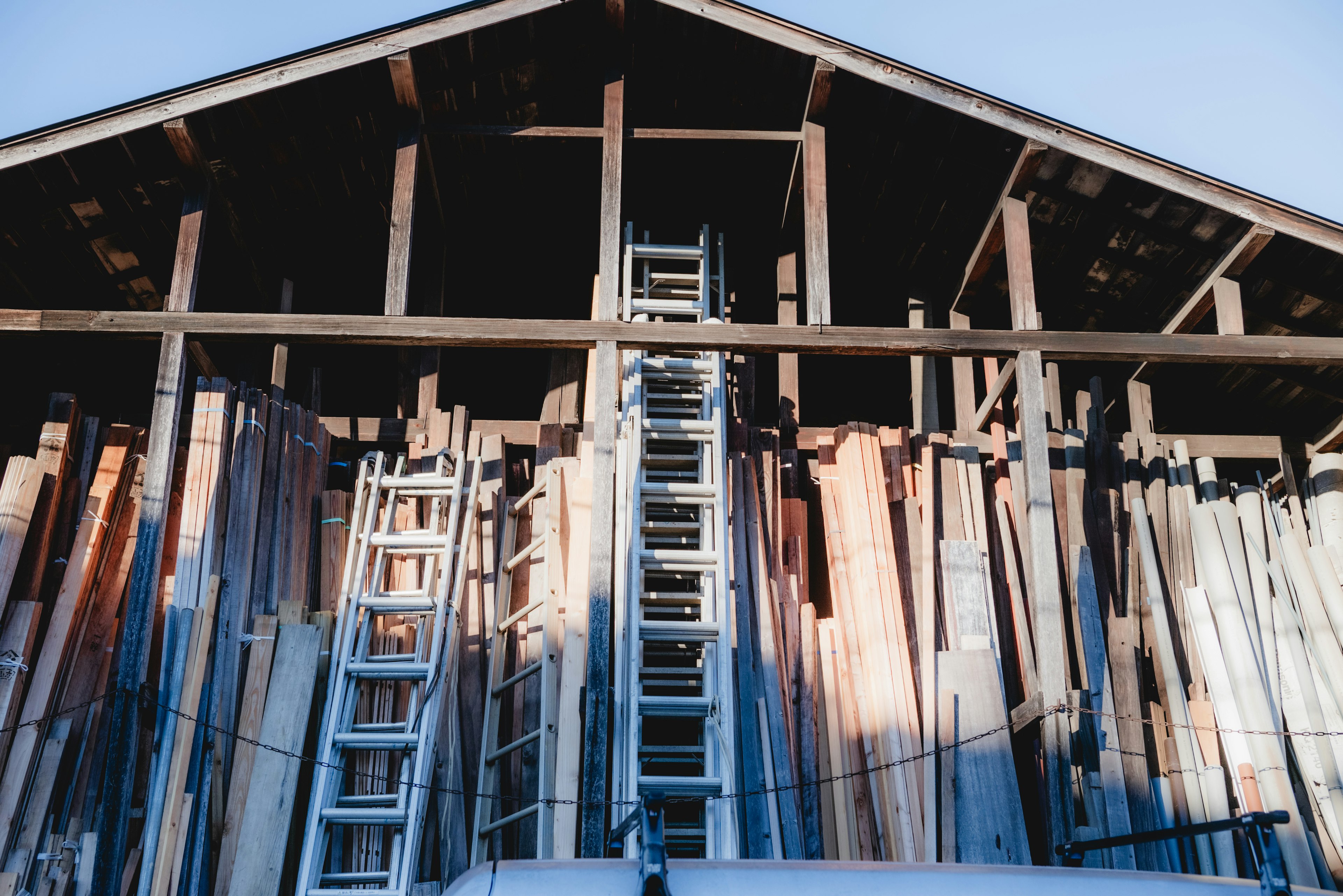 Exterior of a lumber storage building with stacked wood and a ladder