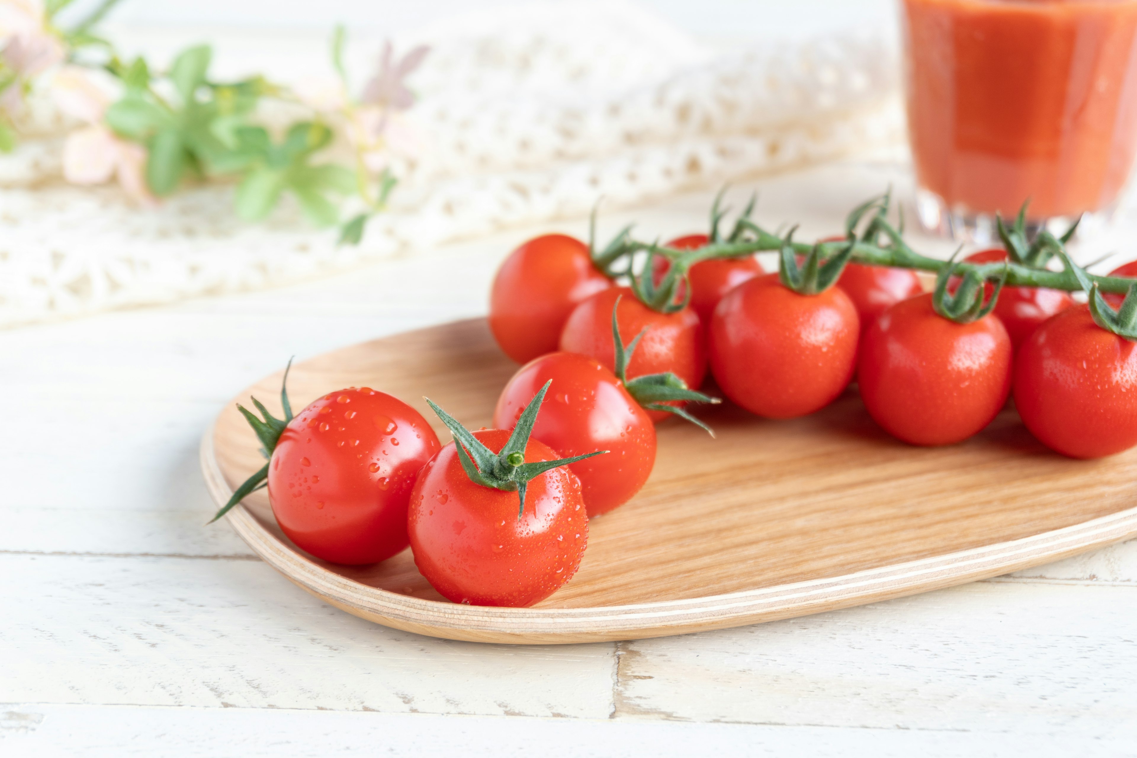 Fresh cherry tomatoes arranged on a wooden plate with a glass of tomato juice